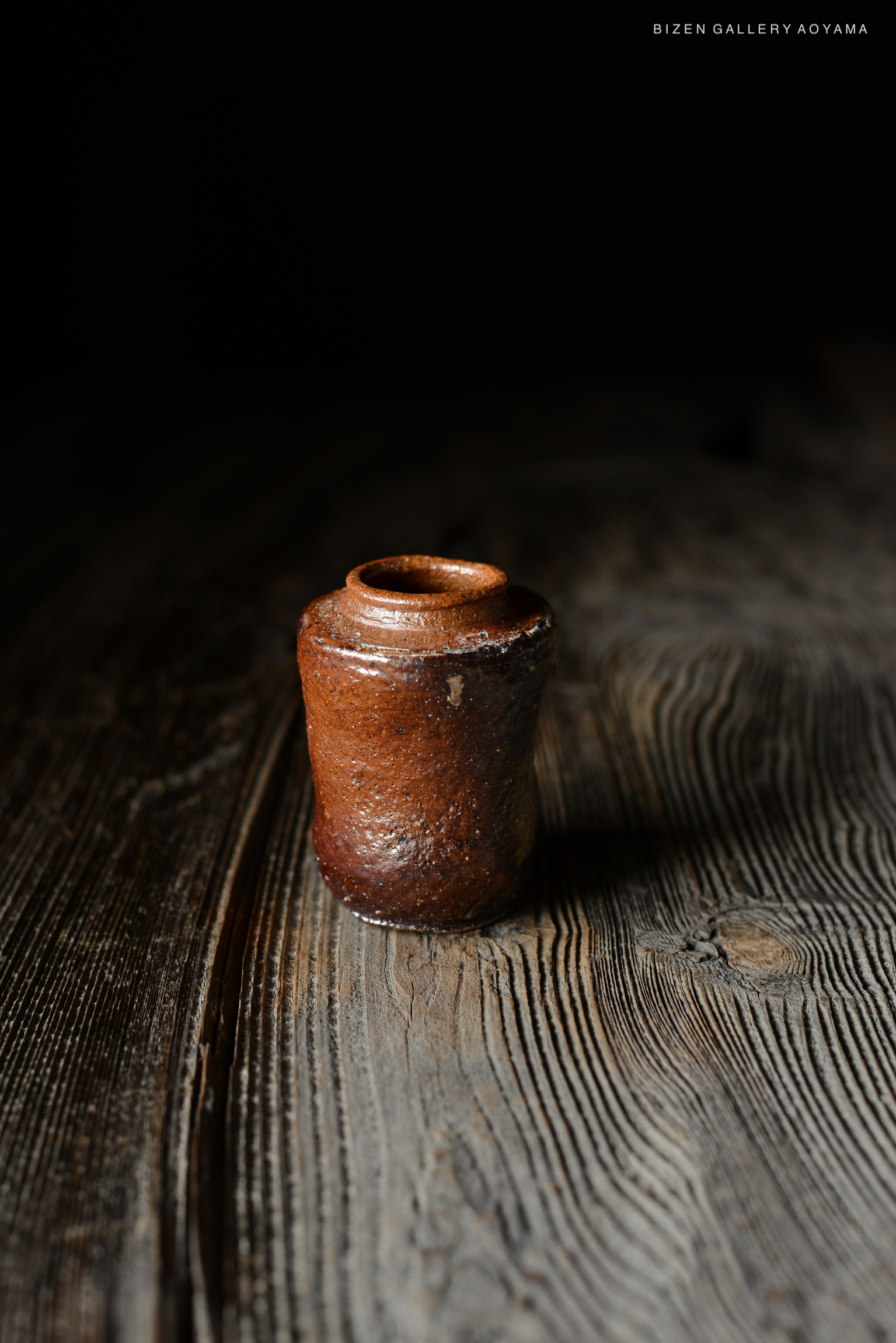 暗い背景の中に置かれた小さな茶色の陶器の壺。