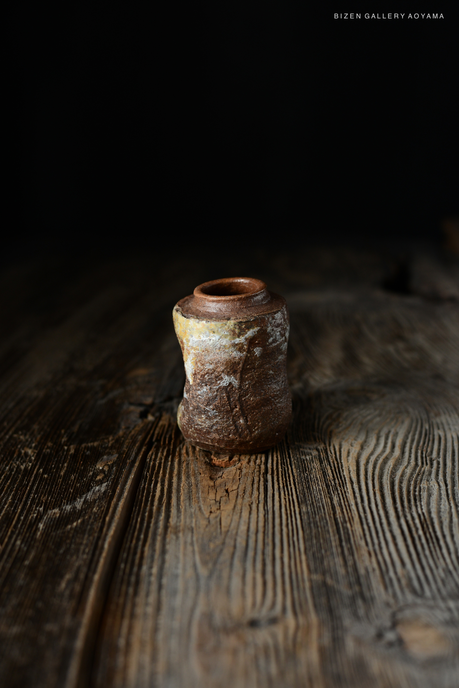 黒い背景の前に置かれた、陶器の一種である独特の形状の小さな壺。木製のテーブルの上に置かれている。