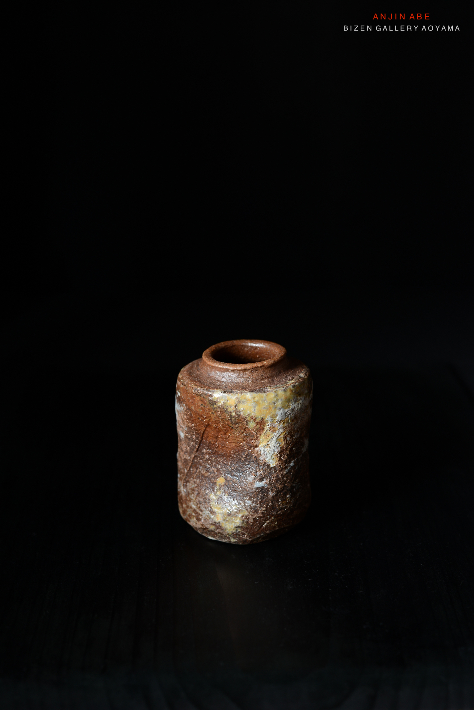 黒い背景の前に置かれた焼き物の壺。色合いは茶色と黄色で、自然なテクスチャーが特徴。