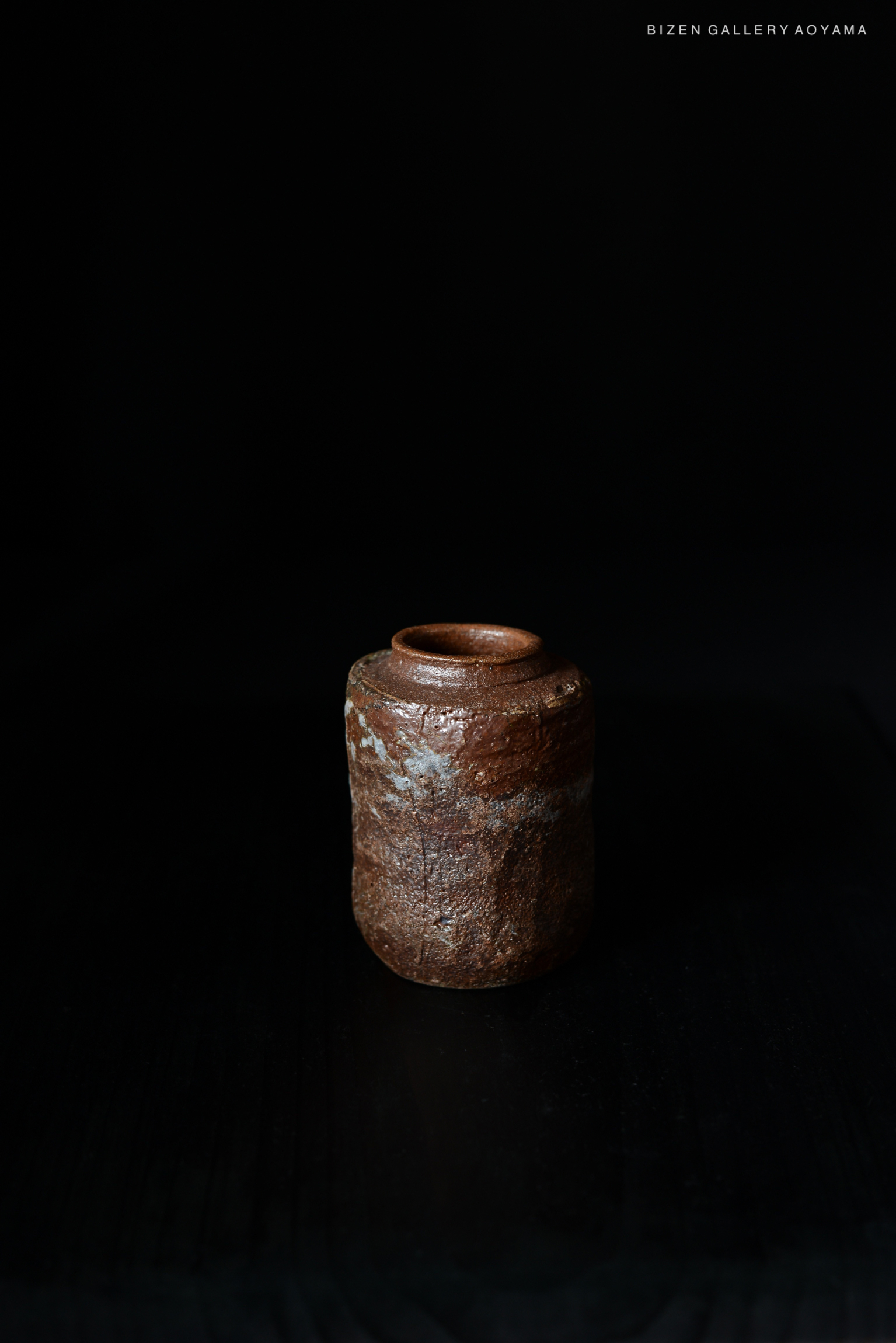 暗い背景の前に置かれた、独特な形状の焼き物。陶器は茶色で、少し凹凸があり、上部には口があります。