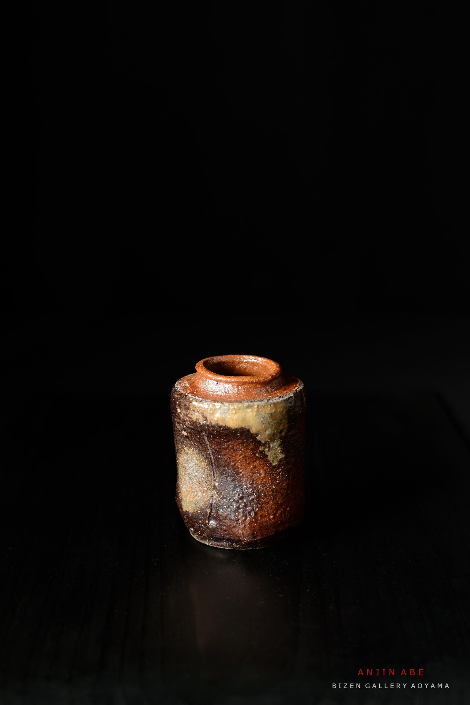 黒い背景の前に置かれた、質感のある焼き物の小さな瓶。