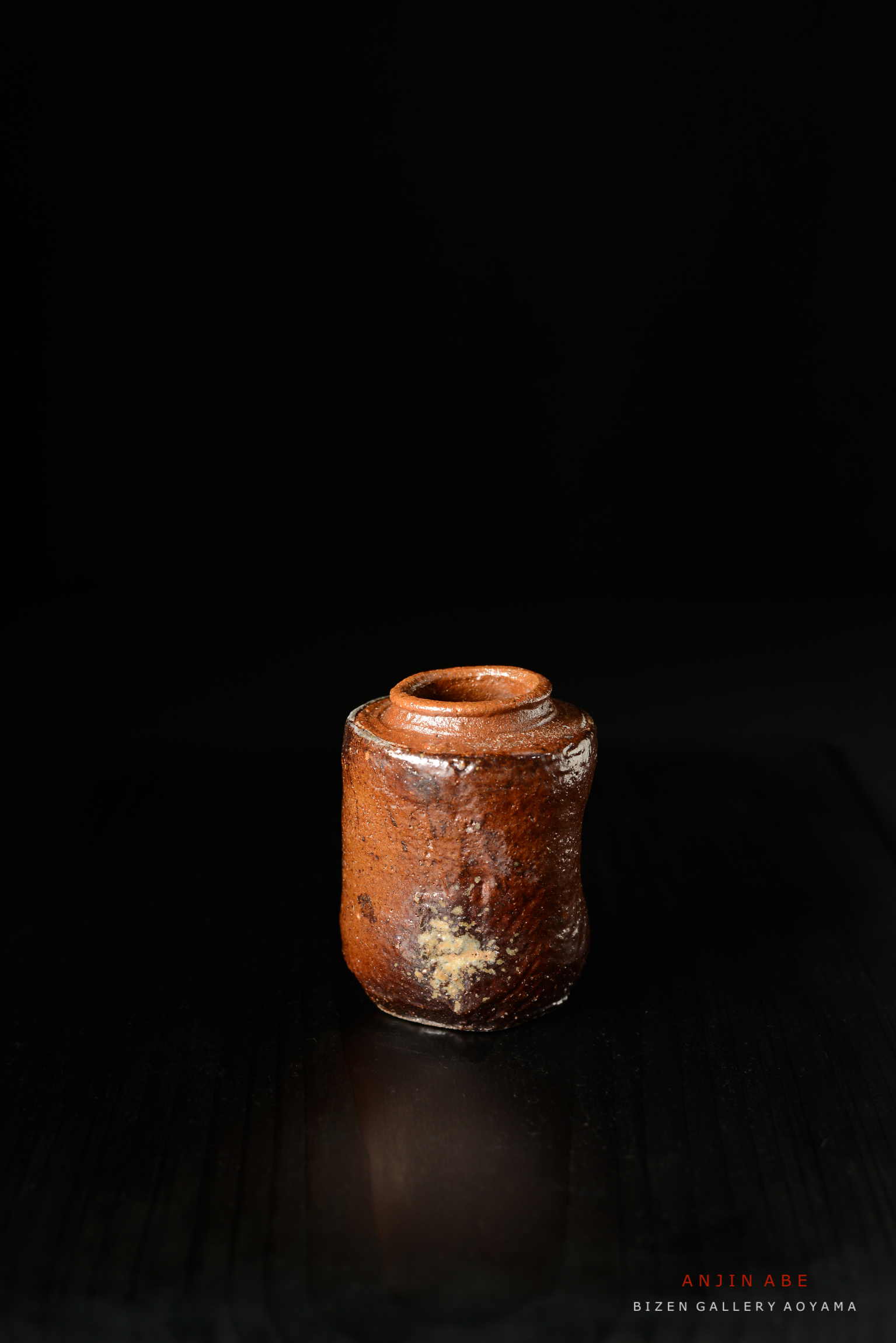 黒背景の上に置かれた焼き物の壺、茶色の釉薬が施されている。
