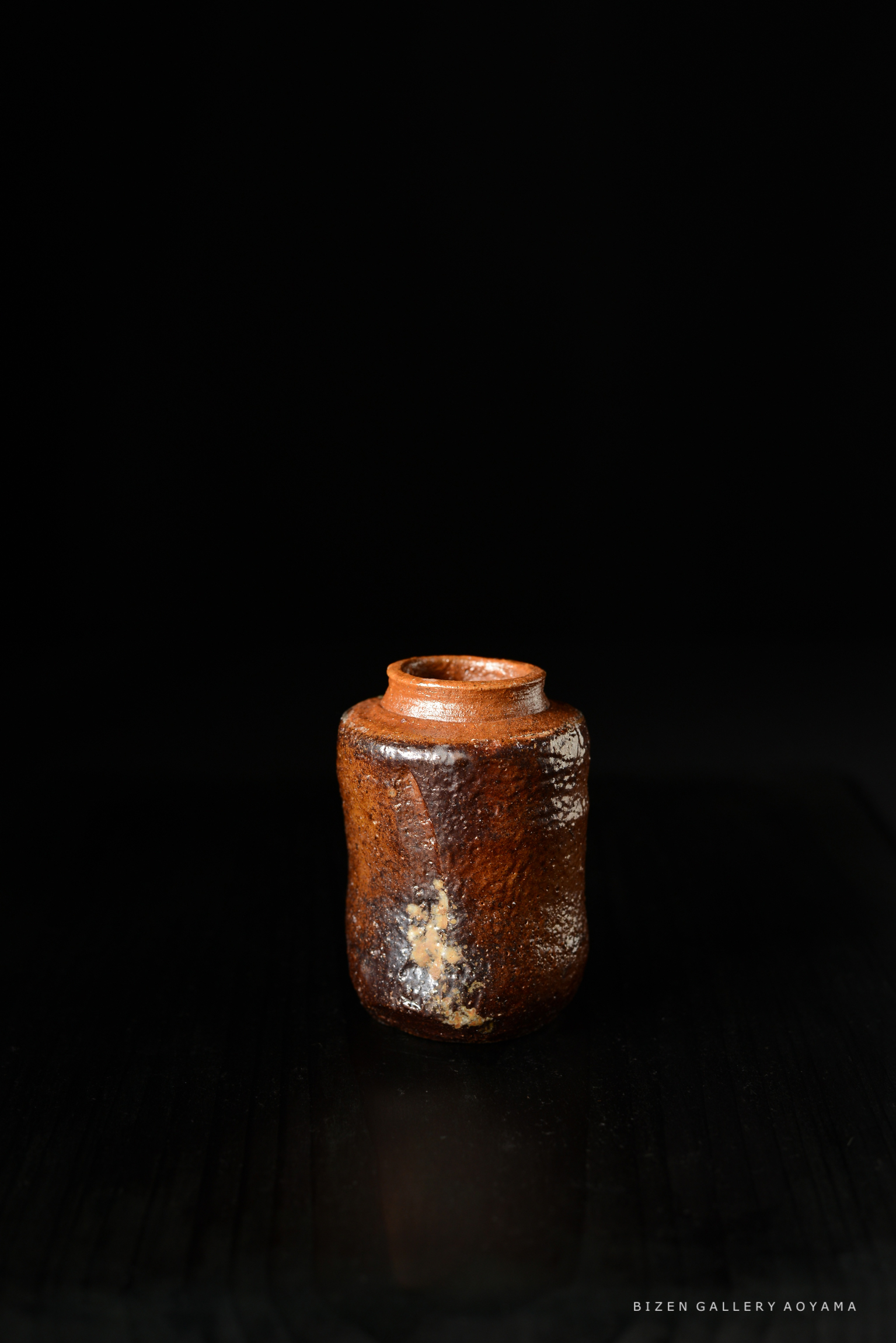 黒い背景に置かれた陶製の壺。茶色の色合いで、独特な形状をしている。