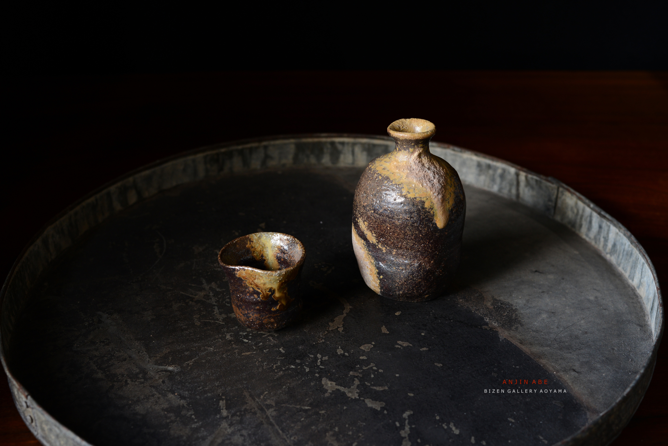 黒い背景の上に置かれた、独特の形状と色合いを持つ壺とカップの陶器。