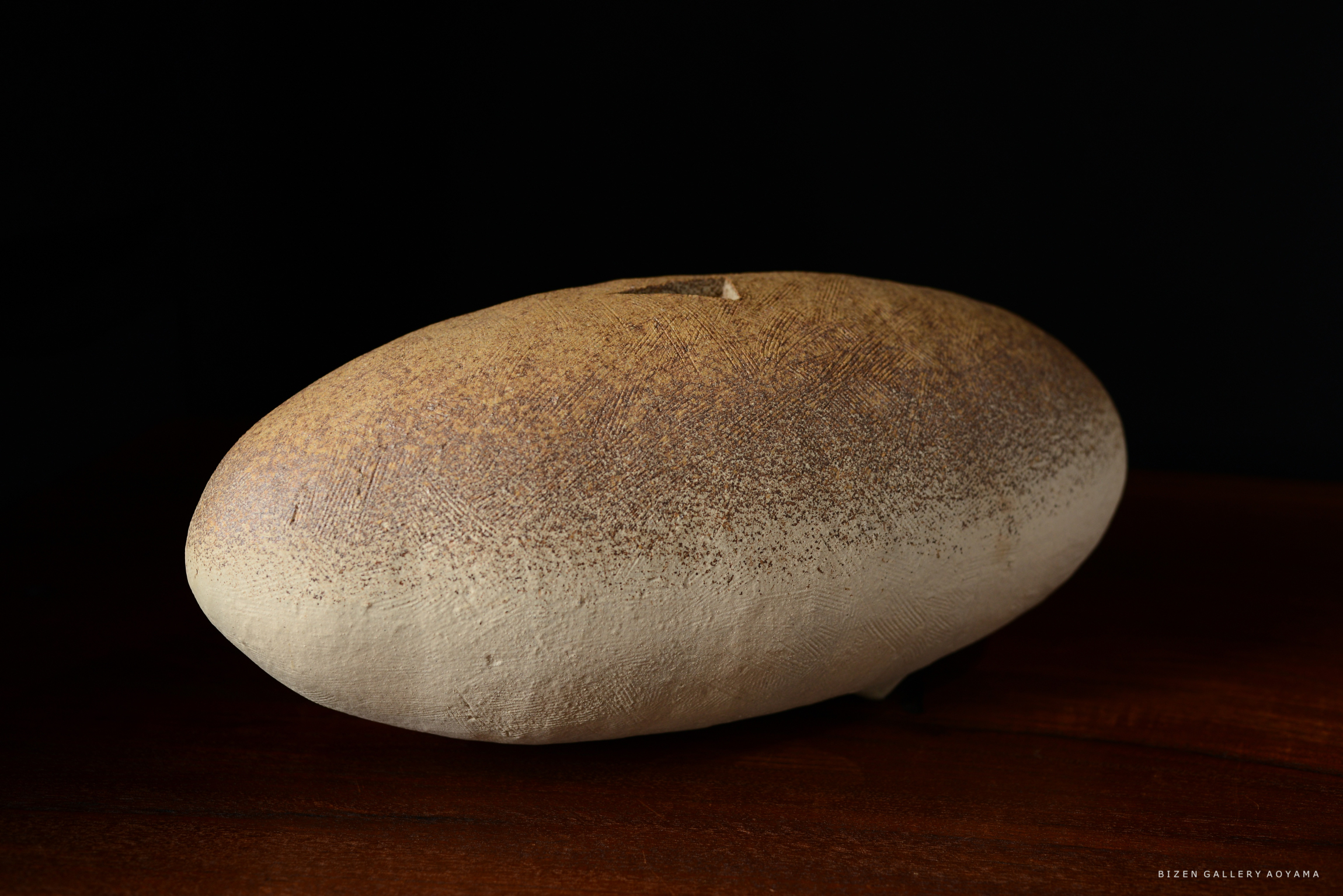 素朴な質感の陶器のオブジェ、茶色い表面が特徴的で、暗い背景に置かれている