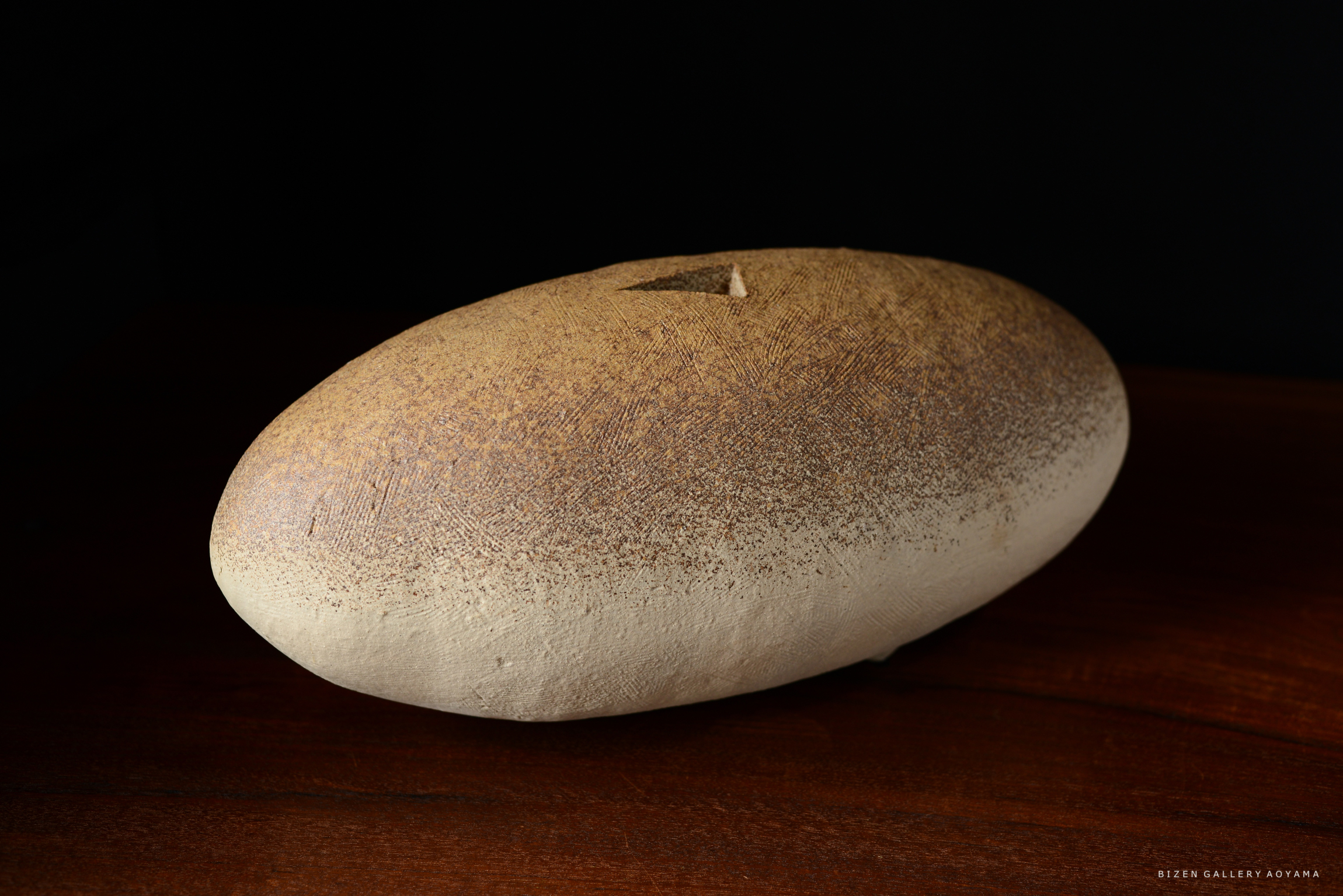 土器のような形状の陶器作品。茶色の模様が施された滑らかな表面を持ち、暗い背景に置かれている。