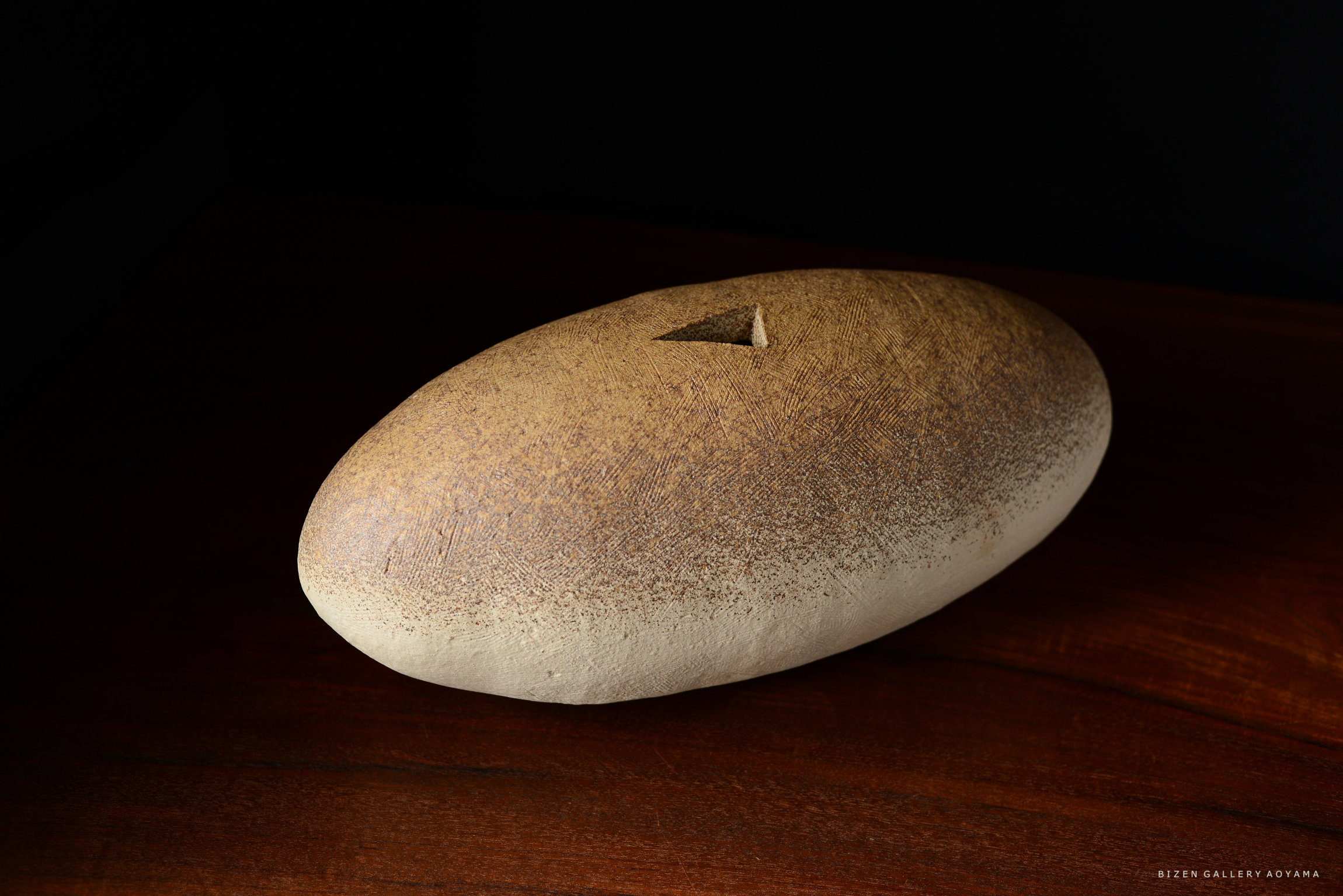 茶色い陶器のオブジェ。表面には細かい模様が施され、中央には小さな三角形の窪みがある。