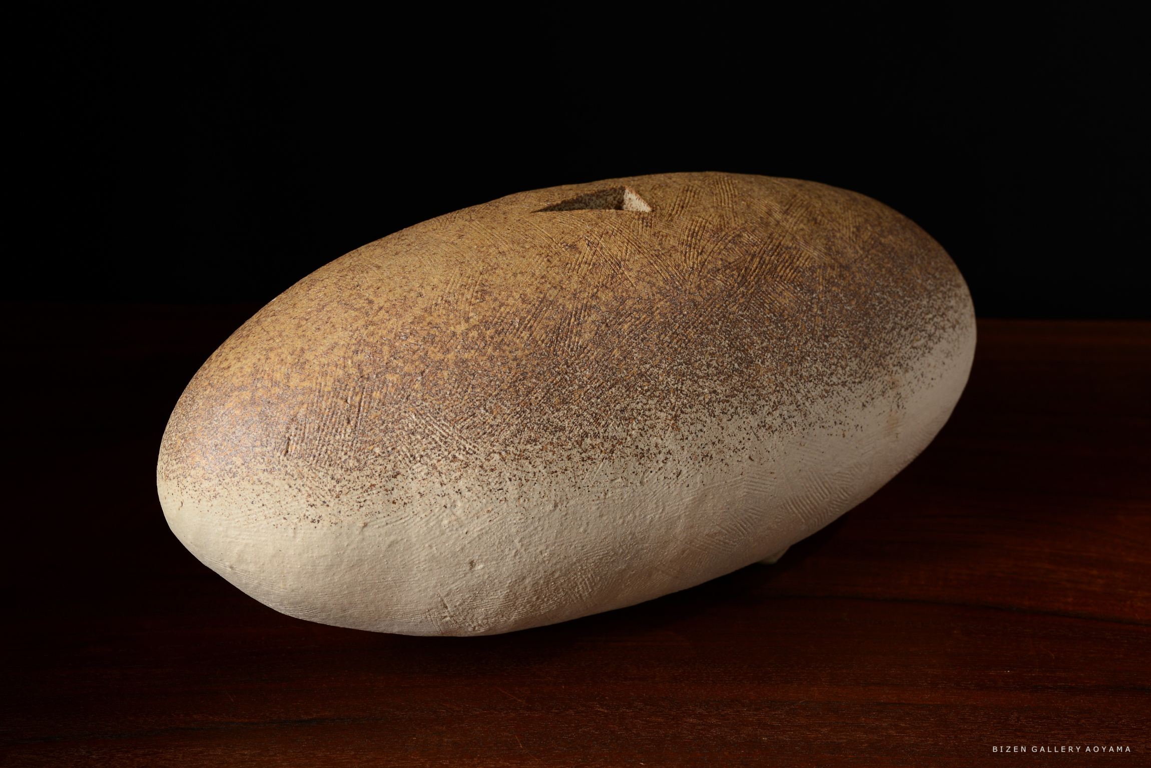 こげ茶色とクリーム色の表面を持つ、平らな楕円形の陶器作品。