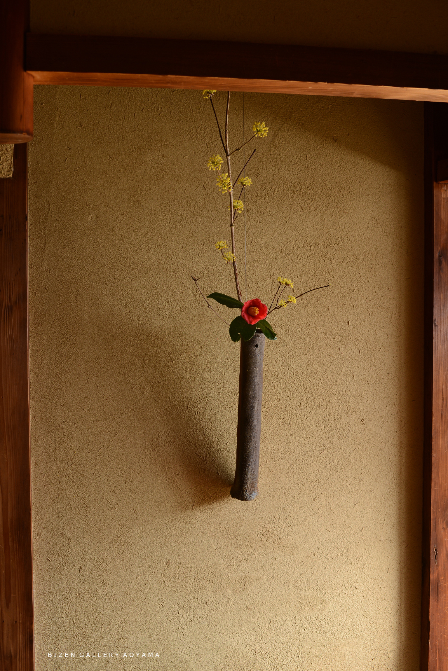 壁に取り付けられた木製の花瓶に黄色い花と赤い花が生けられている様子