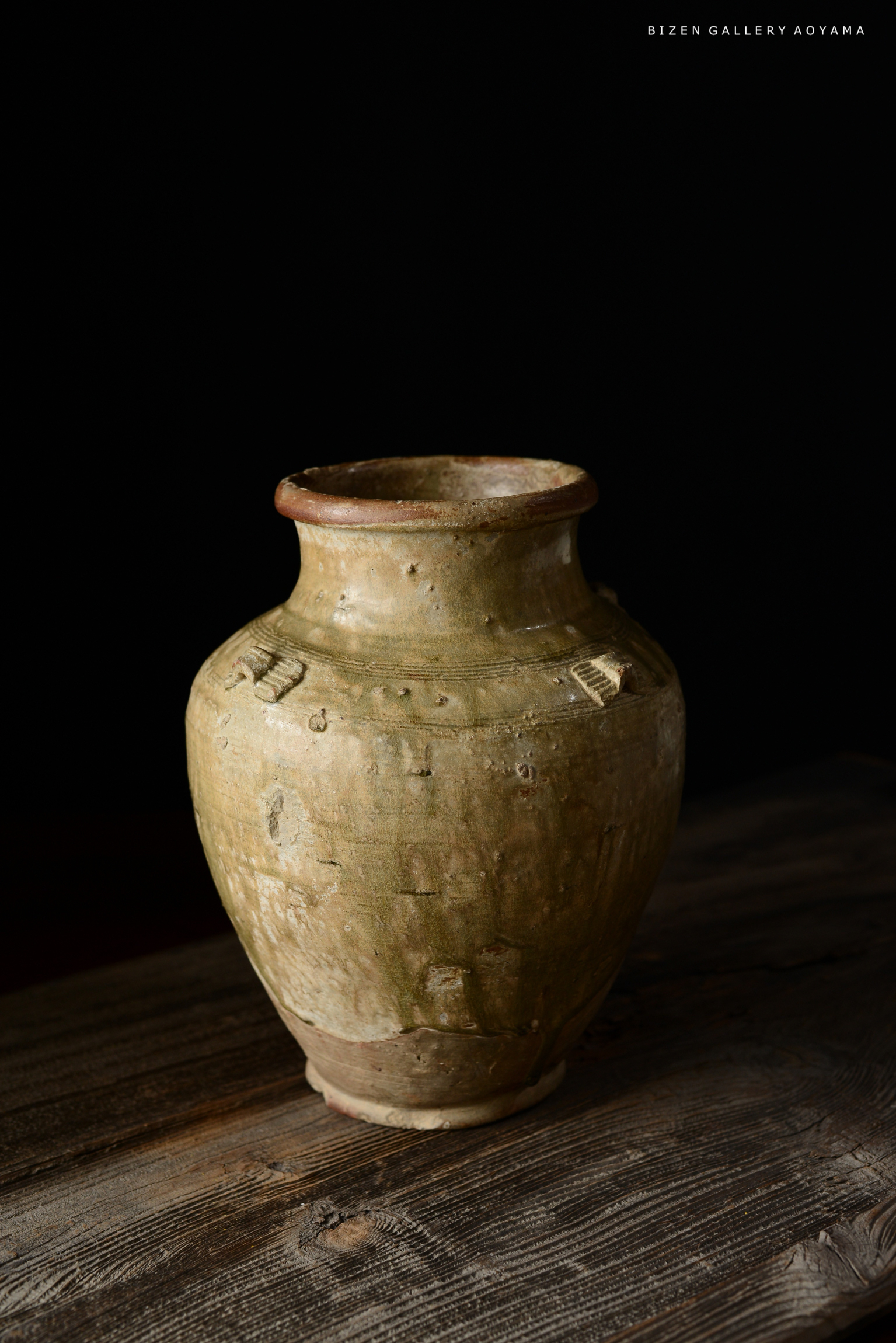 木のテーブルの上に置かれた古い陶器の壺。背景は黒。