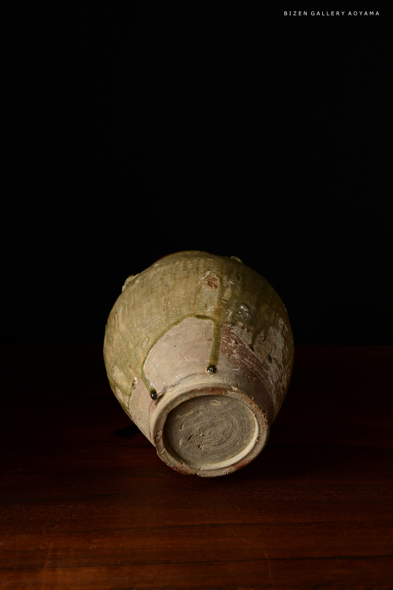 黒い背景に置かれた、底向きの備前焼の壺