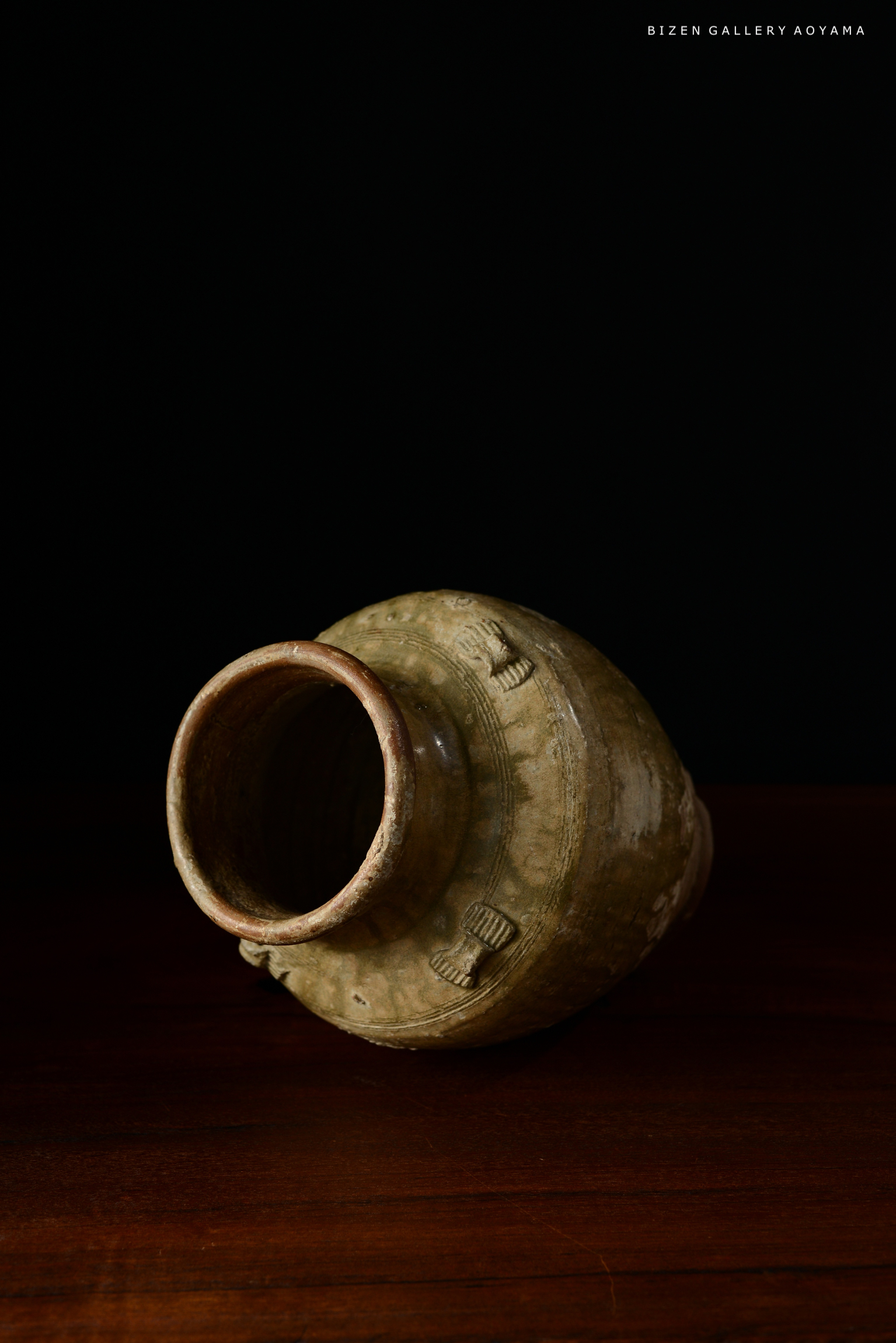 黒い背景の上に置かれた陶器の壺。壺は傾いており、テクスチャーと装飾が視覚的に印象的。