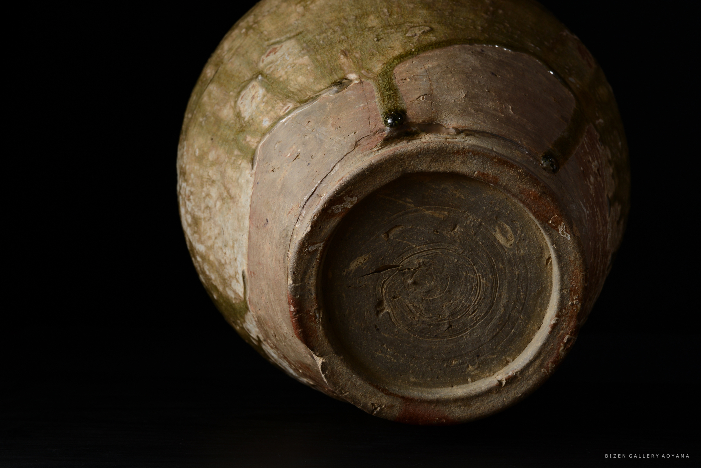 土器の底面が見える画像。黒い背景に対して、土の質感と色合いが際立っている。