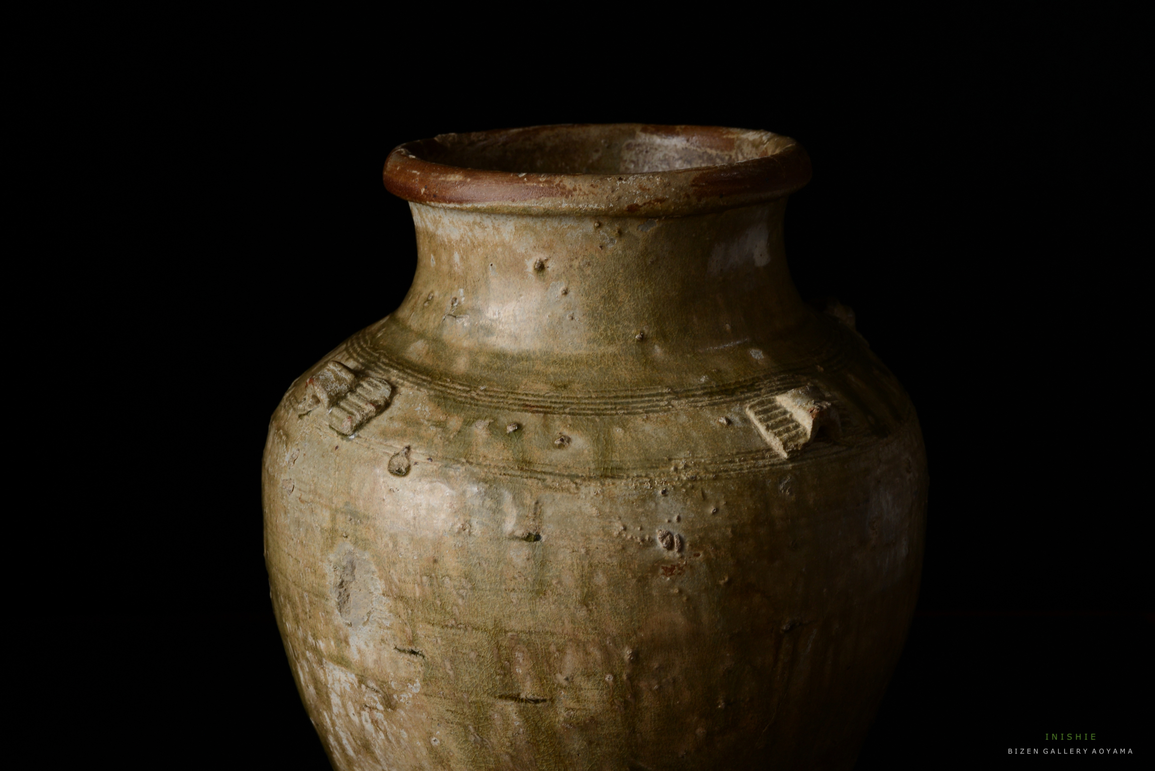 黒背景に置かれた古代の陶器の壺。表面に模様や凹凸があり、口が広がっている。