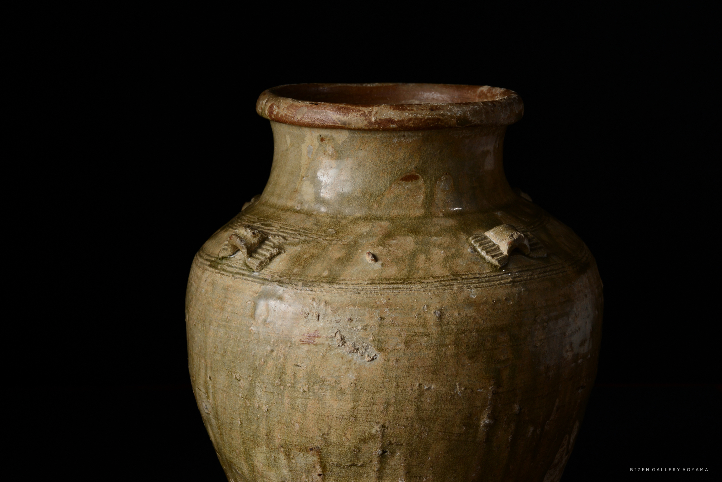 黒バックに置かれた土製の壺。壺の口は広く、側面には模様が施されている。