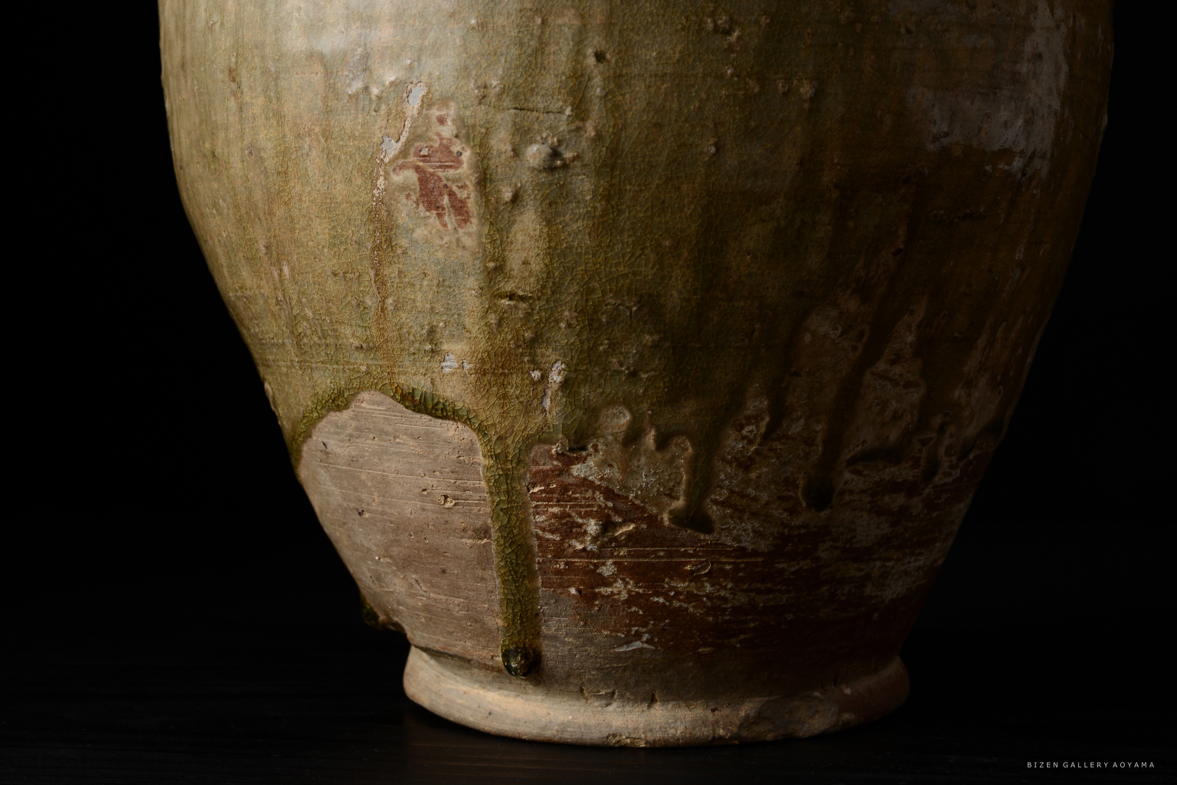 古い陶器の一部がクローズアップされており、土の質感と緑色の釉薬が流れ落ちる様子が見える