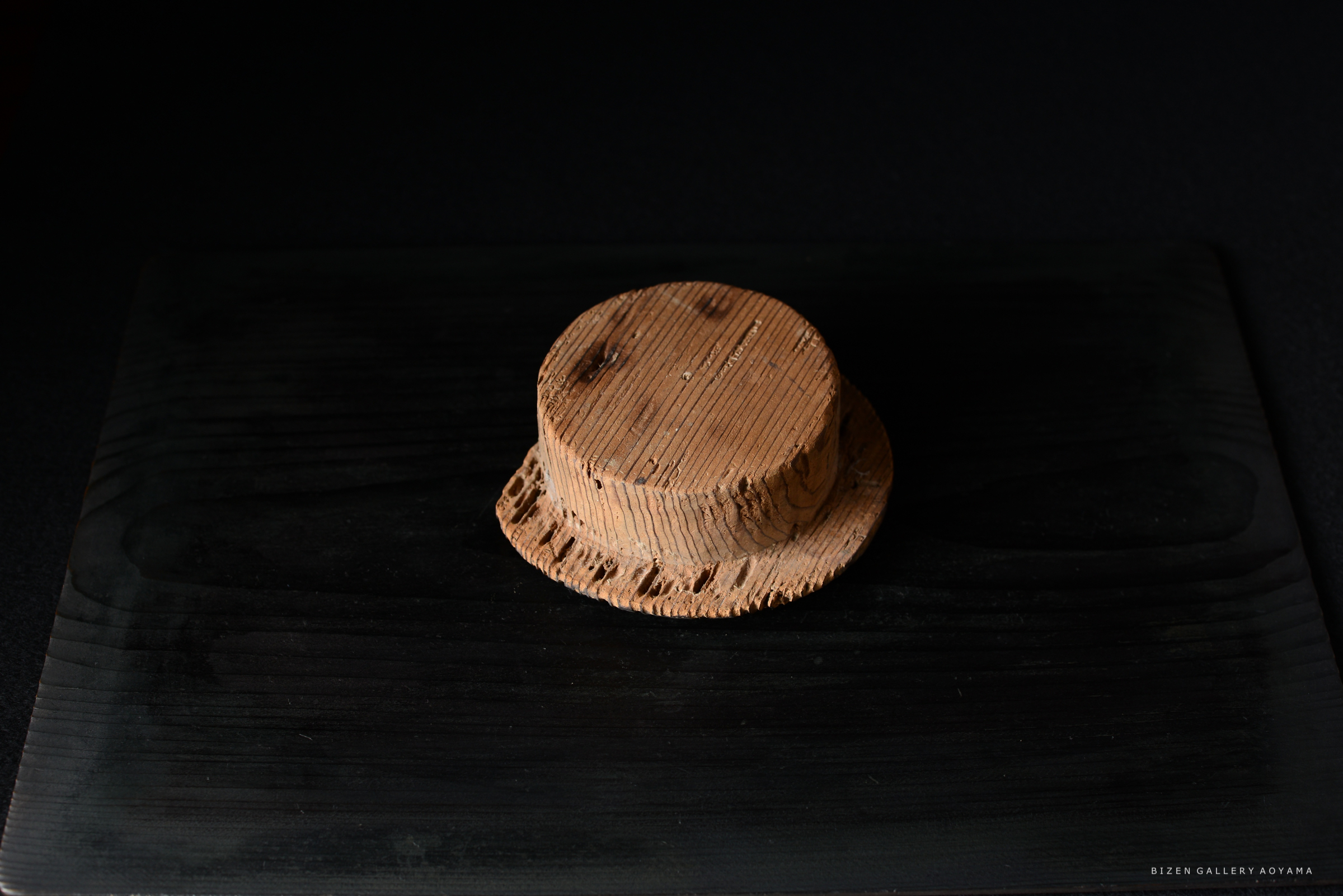 黒い背景の上に置かれた、木材の質感を持つ円筒形の作品。