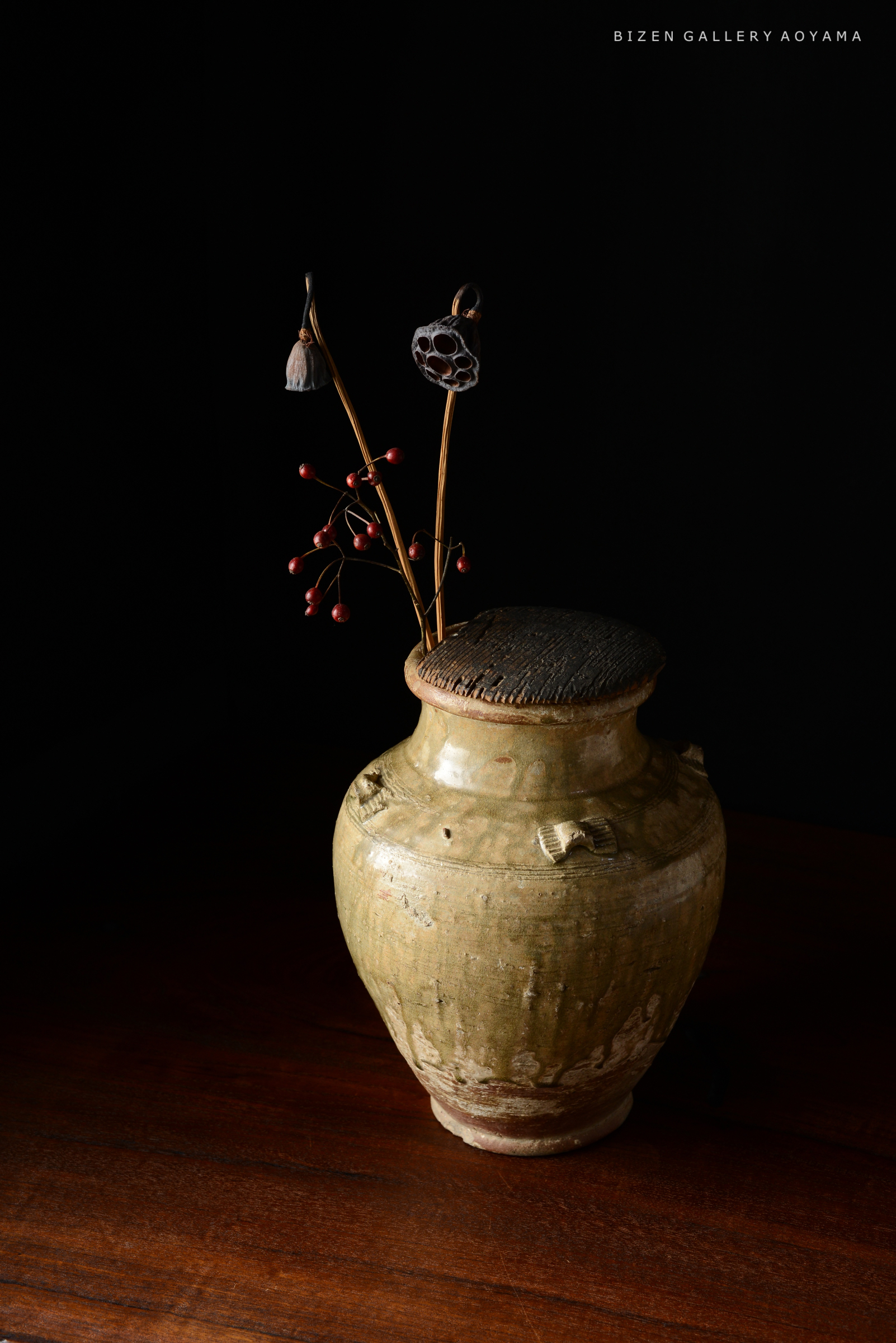 黒い背景に置かれた、装飾された陶器の花瓶と植物の配置。