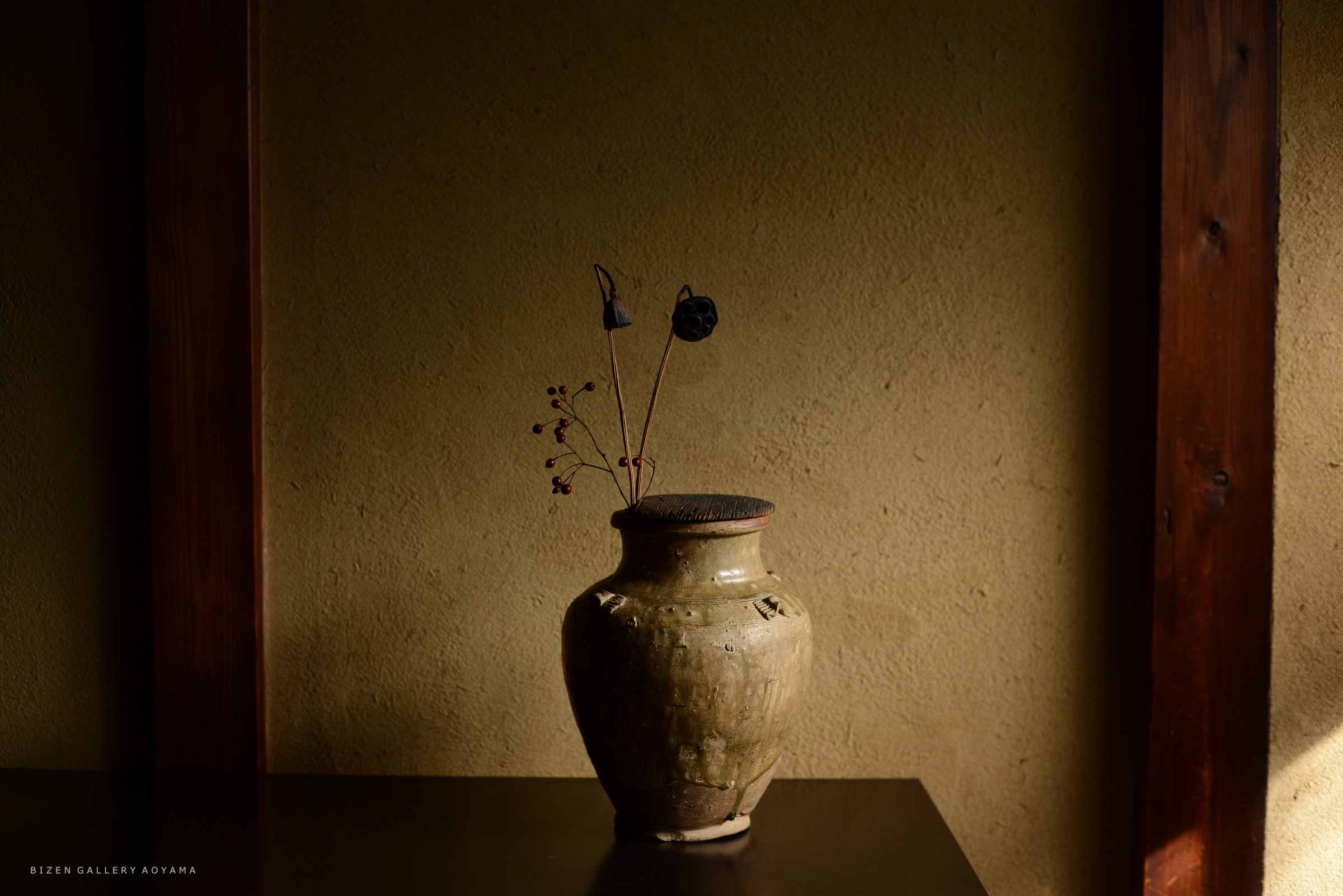 木製のテーブルの上に置かれた陶器の花瓶と、 dried flowers.