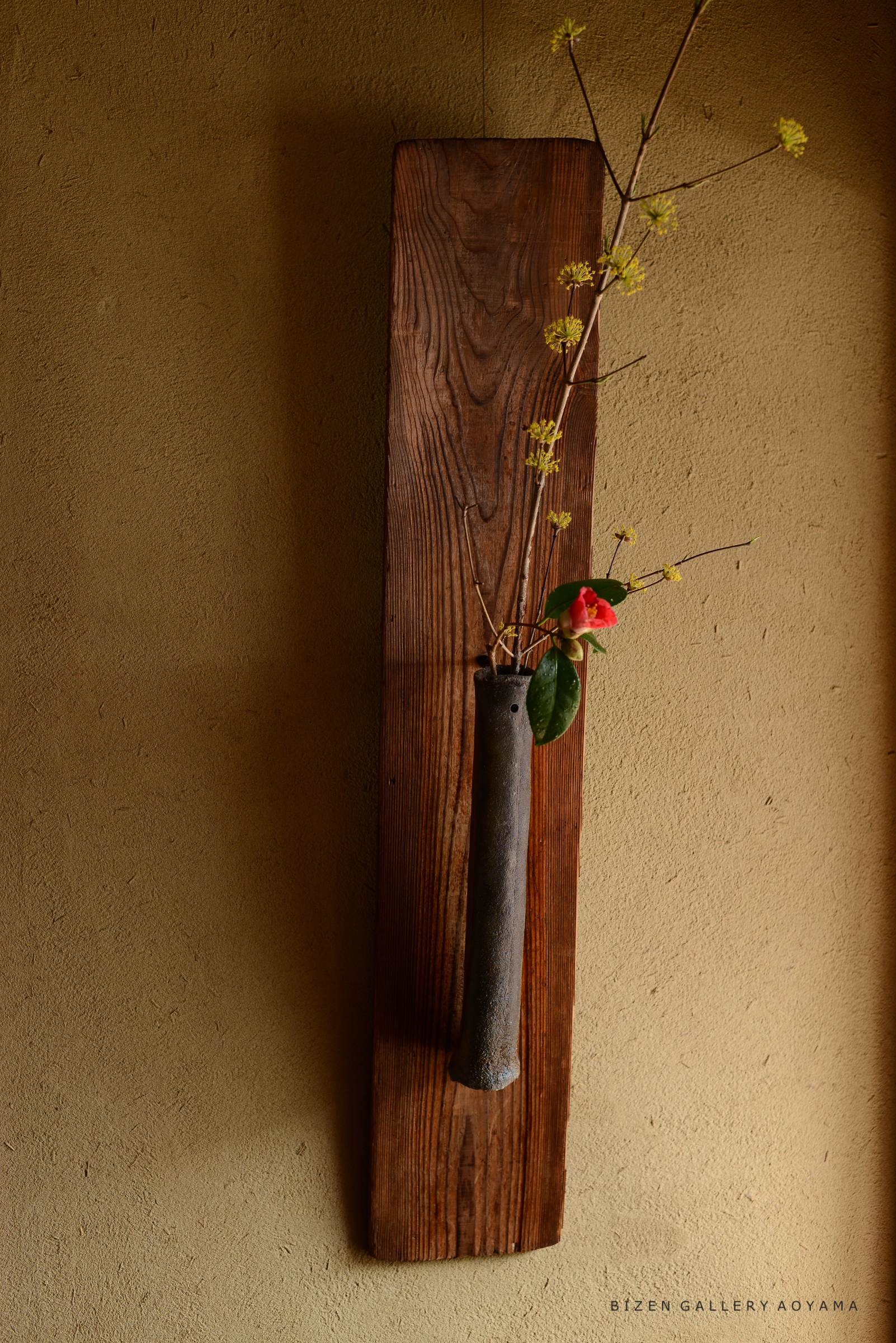 木製の板に陶器の花瓶が取り付けられ、花と葉が挿してあるインテリアの画像