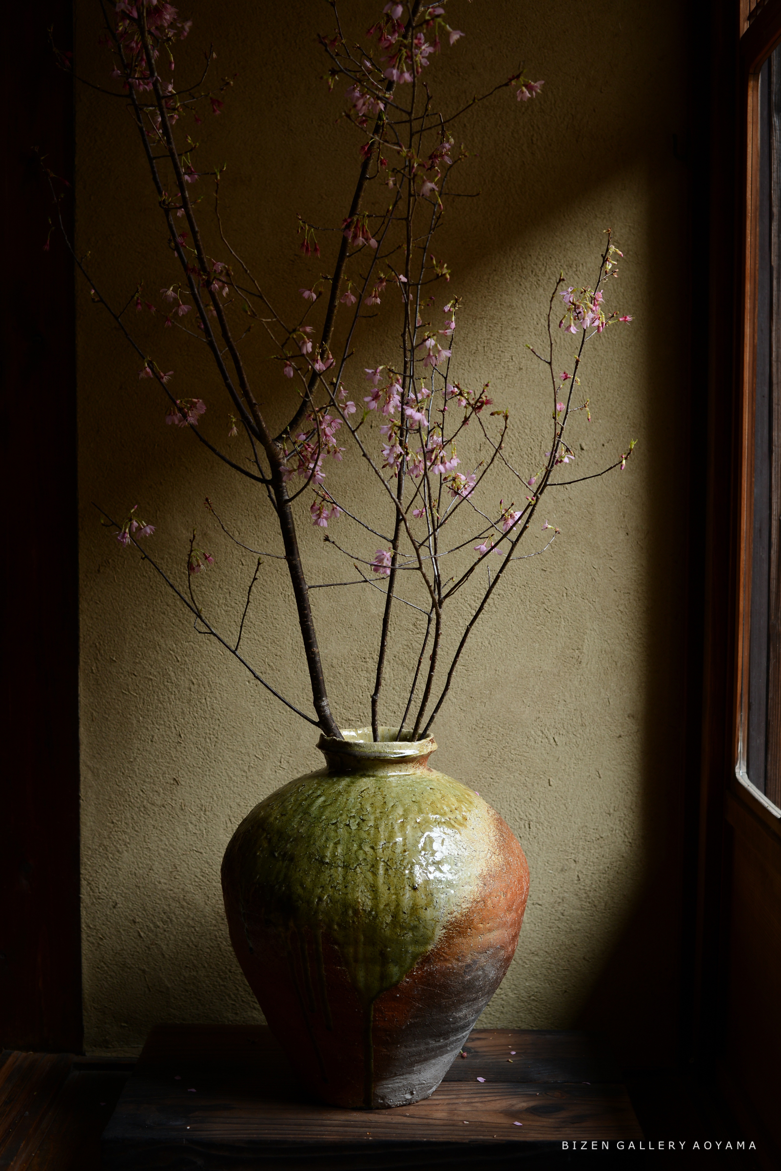 生け花の陶器の花瓶に咲く桜の枝が立てられた室内の風景。