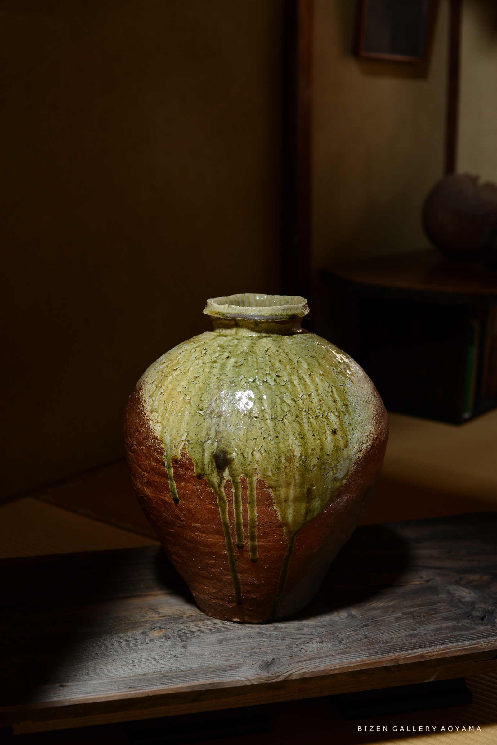 緑色の釉薬が流れ落ちた陶器の壺が、木の台の上に置かれている。