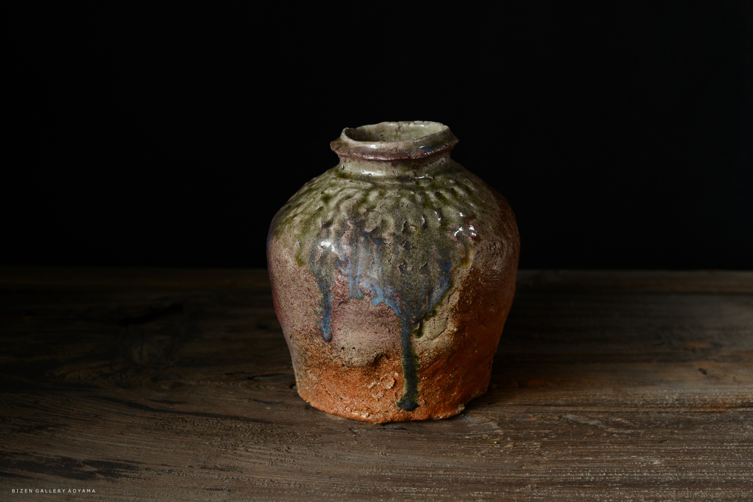 独特な釉薬のかかった丸い陶器の壷が、木のテーブルの上に置かれています。