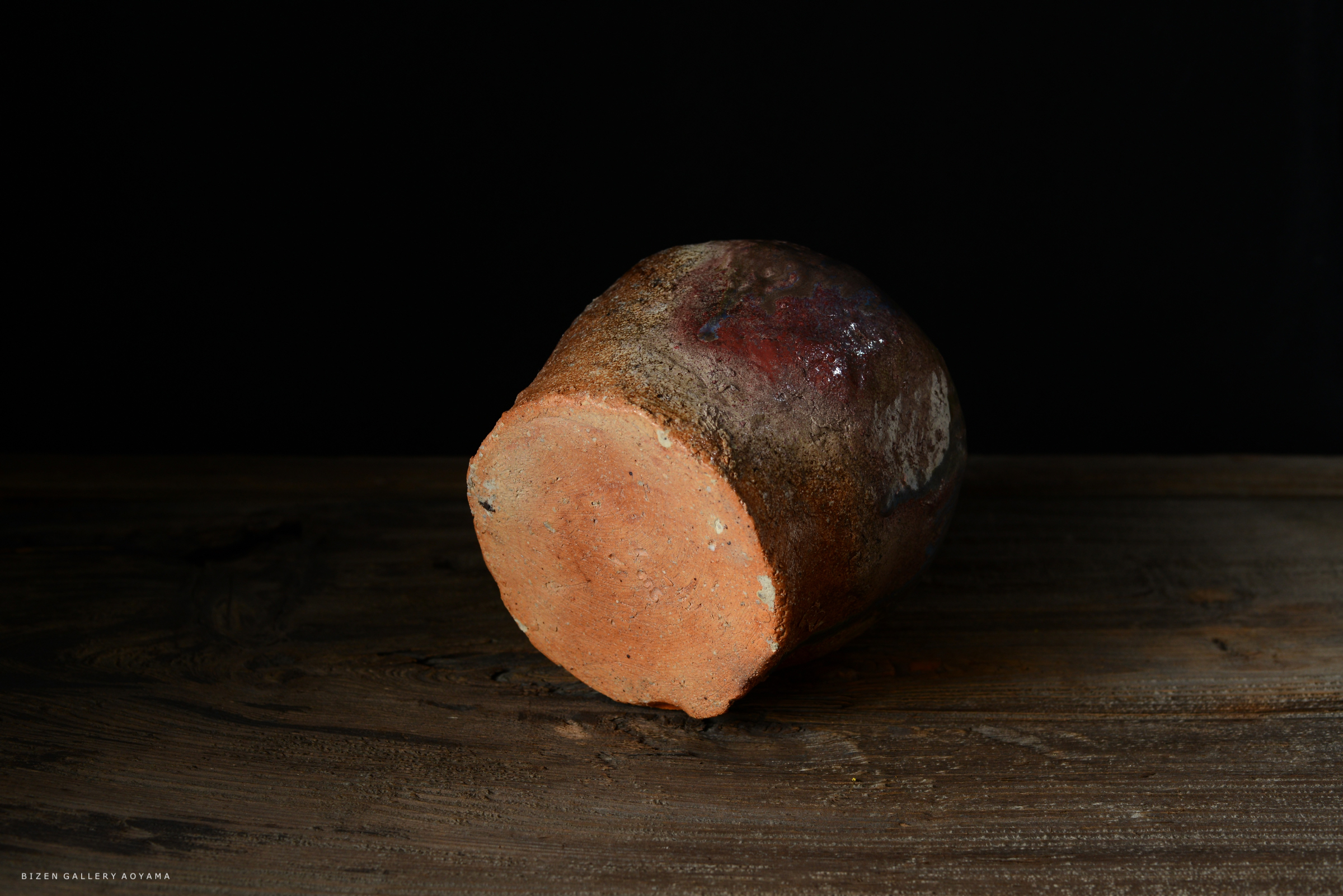 黒背景に置かれた、土の質感を持つ陶器の底面の写真。