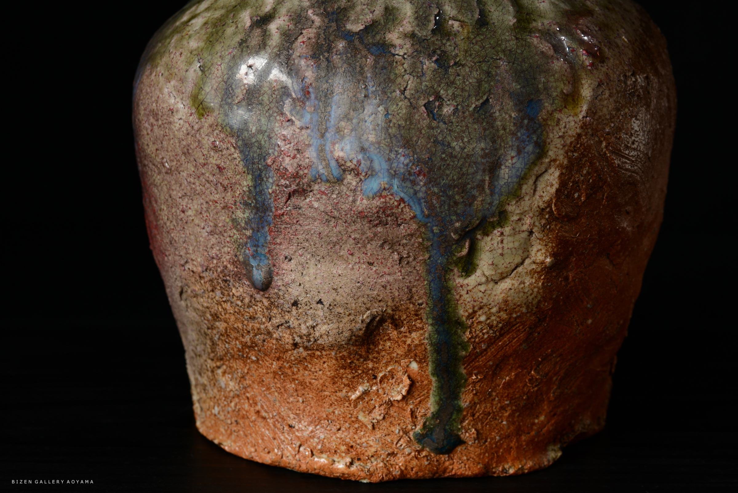 個性的な釉薬がかかった陶器の一部アップ。色彩は緑、青、茶色のグラデーションがあり、表面にはひび割れが見られる。