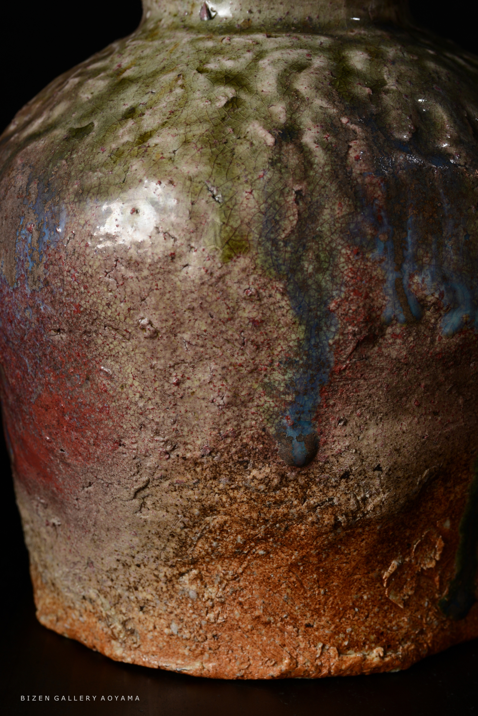 独特な模様と色合いを持つ陶器の近接写真。表面にはひび割れや釉薬の流れが見られ、茶色と緑色が混ざった印象を与える。