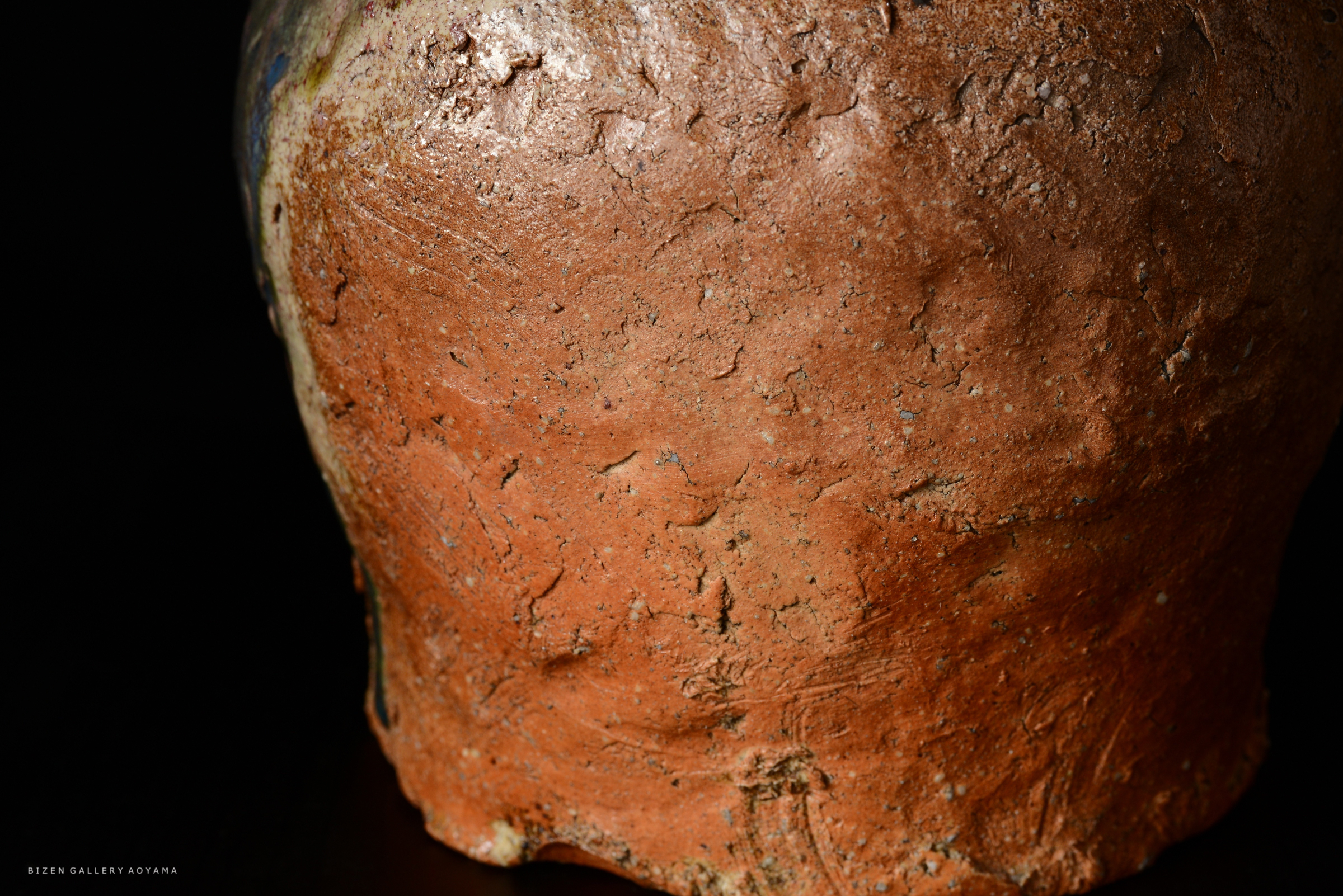 赤土の陶器の側面のクローズアップ。表面には自然なテクスチャーと色合いがあり、暗い背景に映えている。