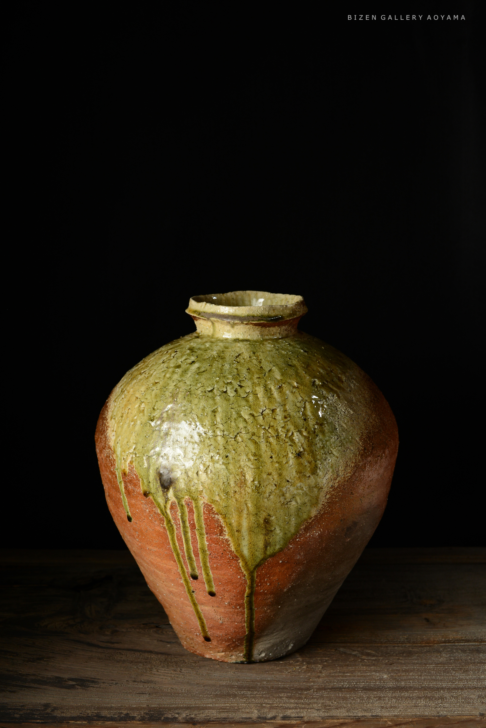 黒い背景に置かれた、緑と赤の釉薬が施された素焼きの壺。
