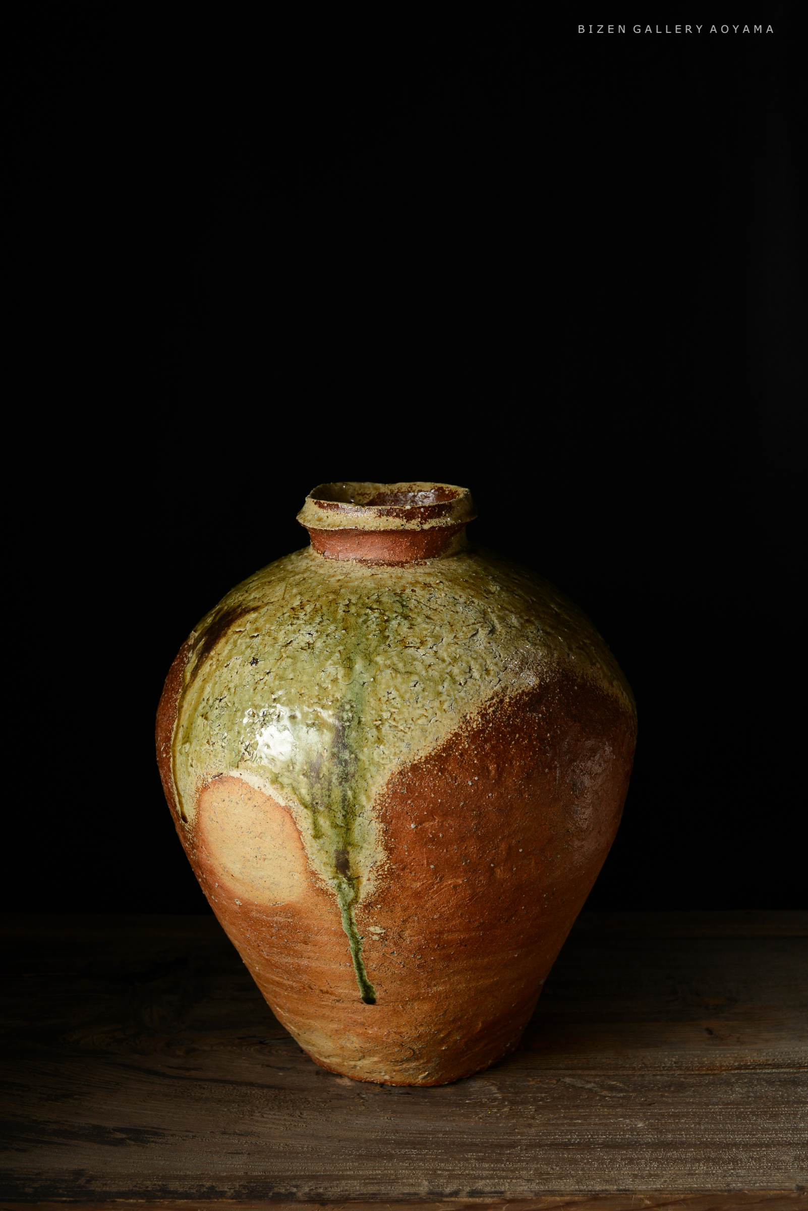 黒い背景に置かれた大きな焼き物の壺。自然な土の色合いと釉薬の滴りが特徴的。