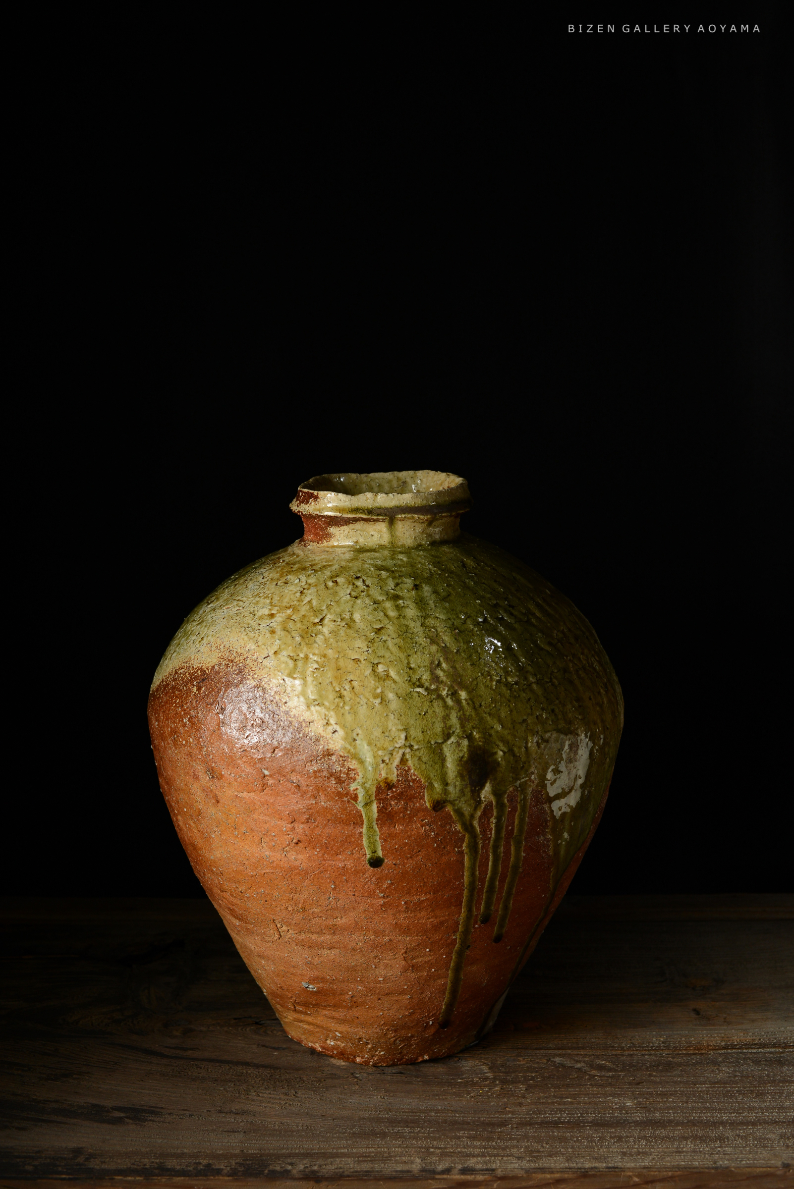 黒い背景の前に置かれた、緑色の釉薬がかかった焼き物の壺