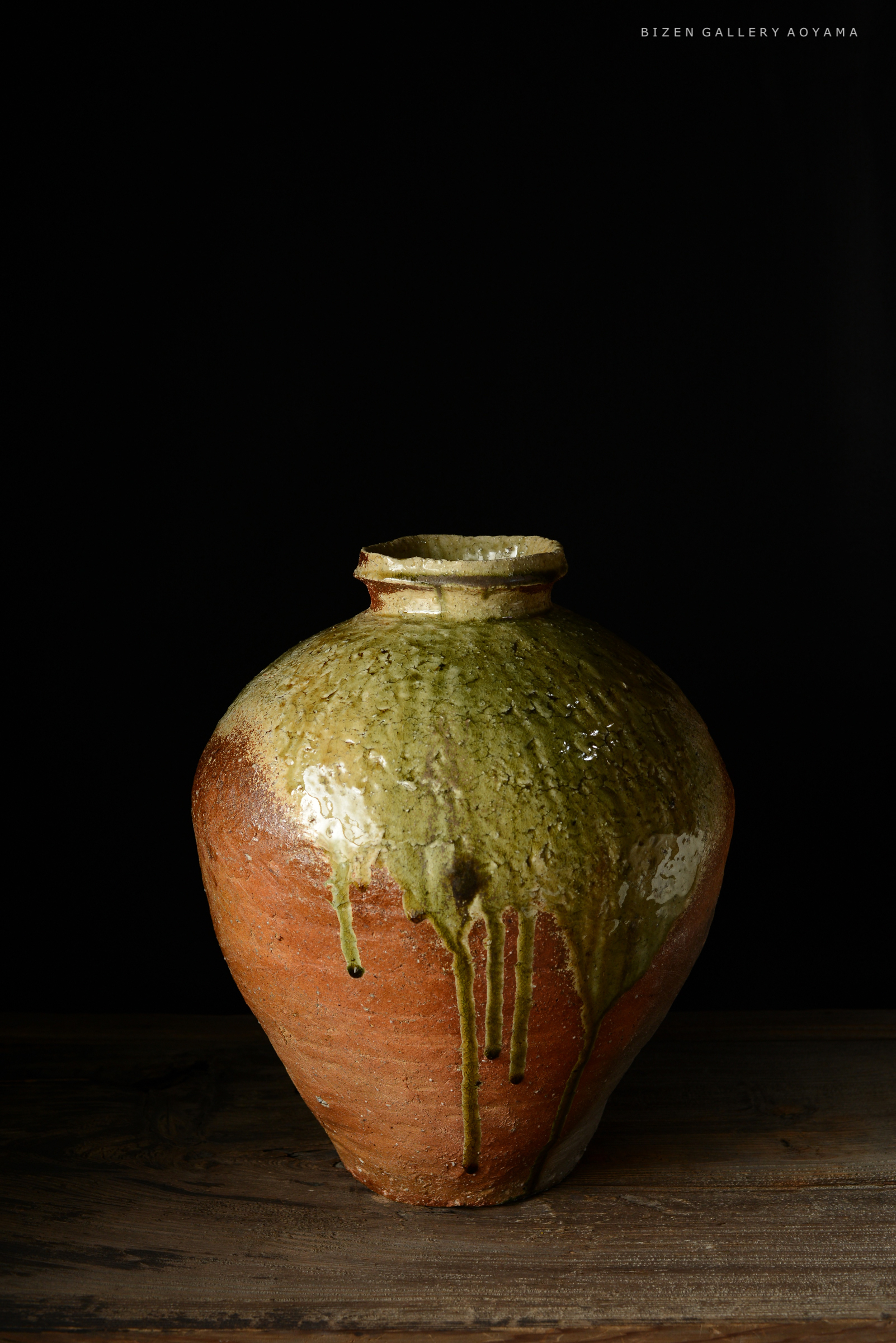 黒い背景に置かれた、緑色の釉薬がかかった丸い陶器の壺。