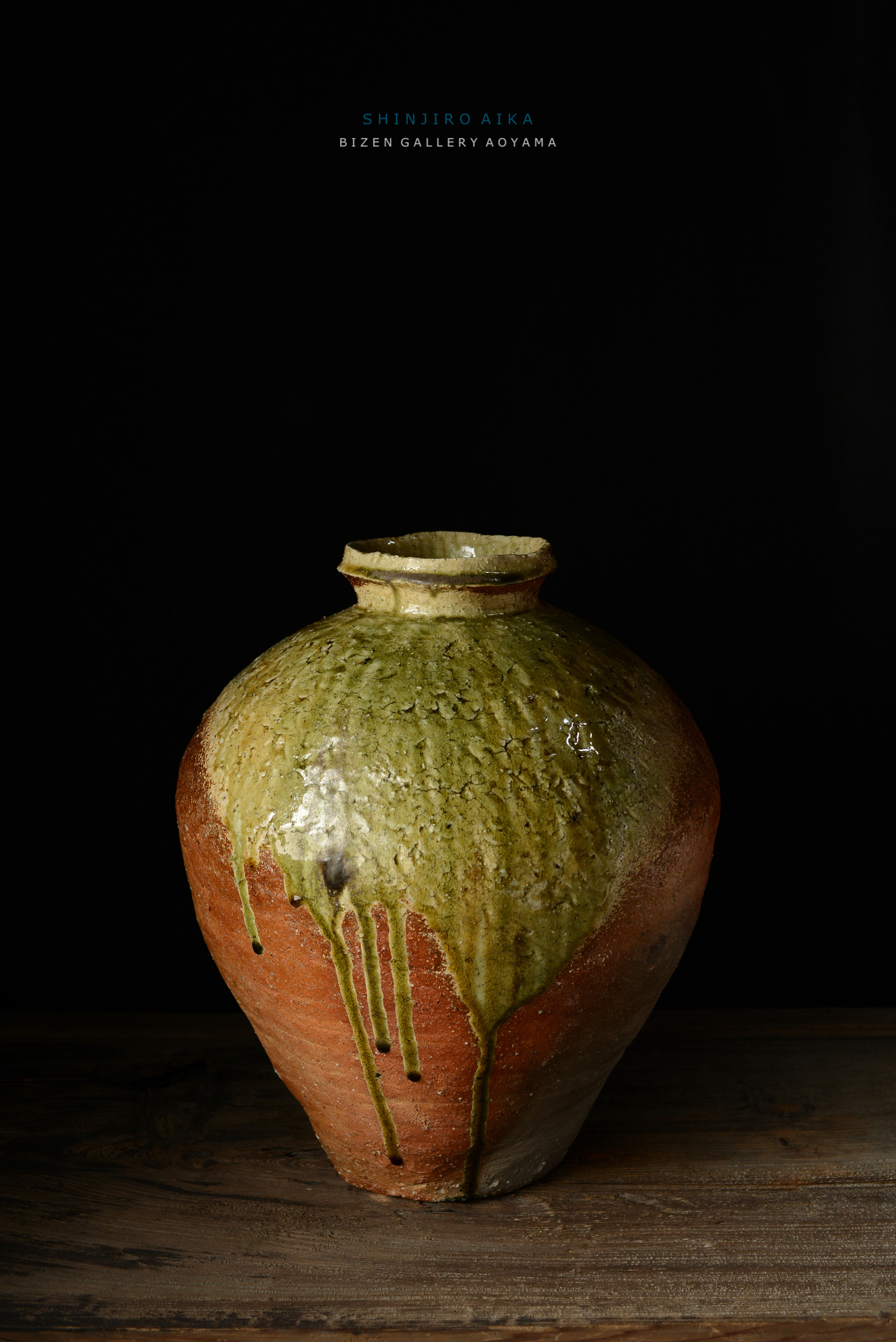 焼き物の壺、緑とオレンジの釉薬が垂れた美しい陶器。背景は黒で、木のテーブルの上に置かれている。