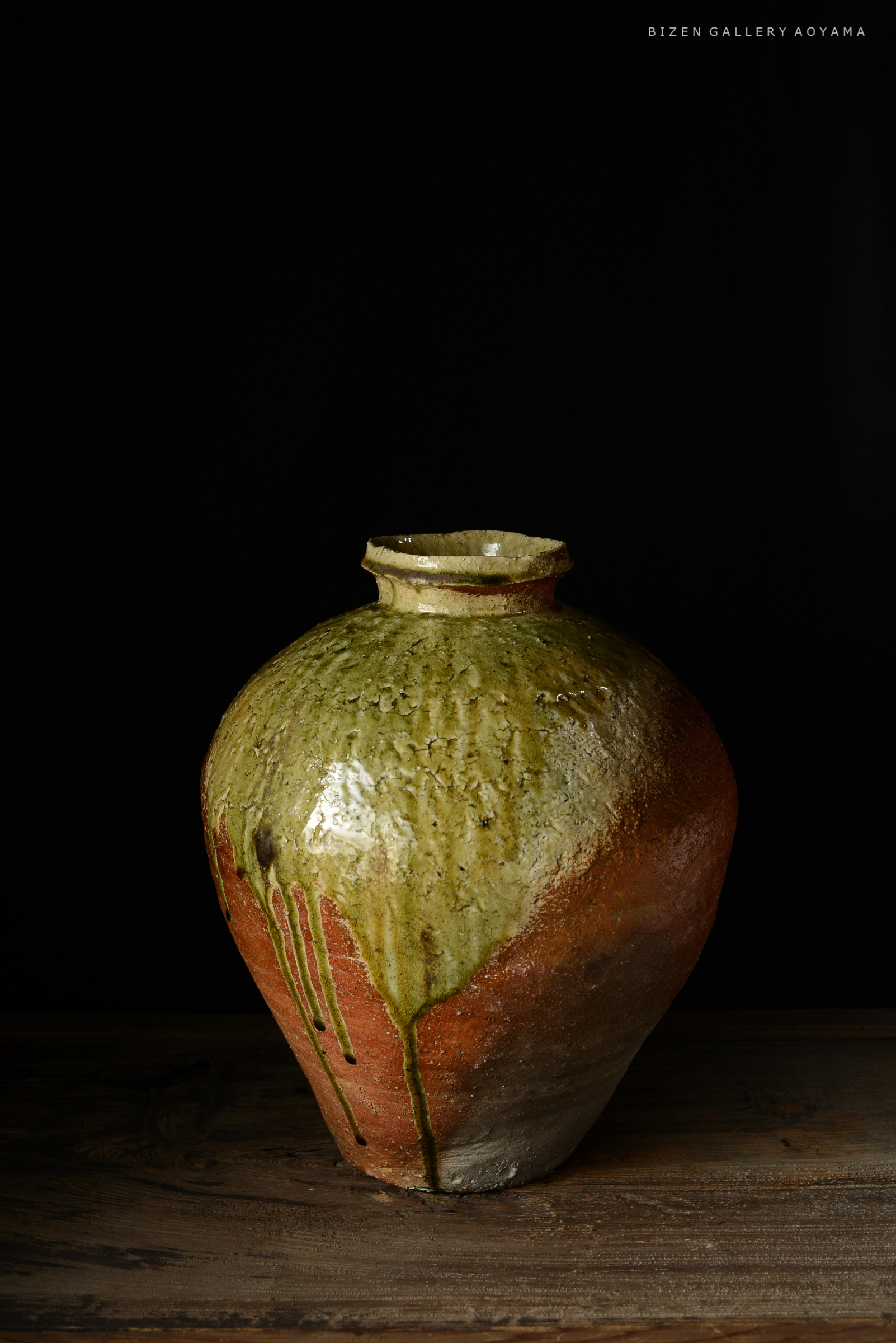 黒い背景の前に置かれた緑と赤の釉薬が施されたビゼン焼の花瓶