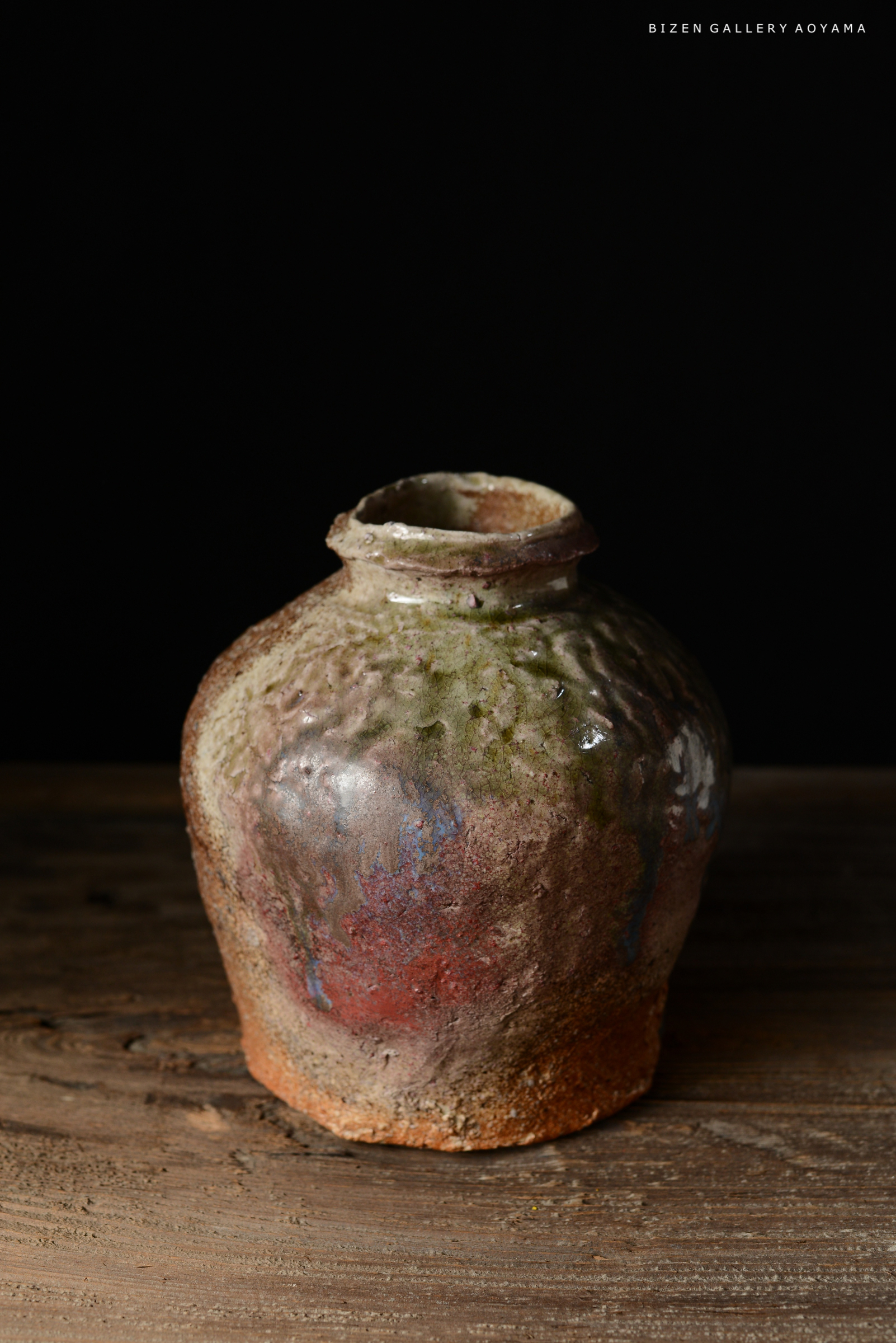 黒い背景の前に置かれた、色彩豊かな表面を持つ焼き物の壺。