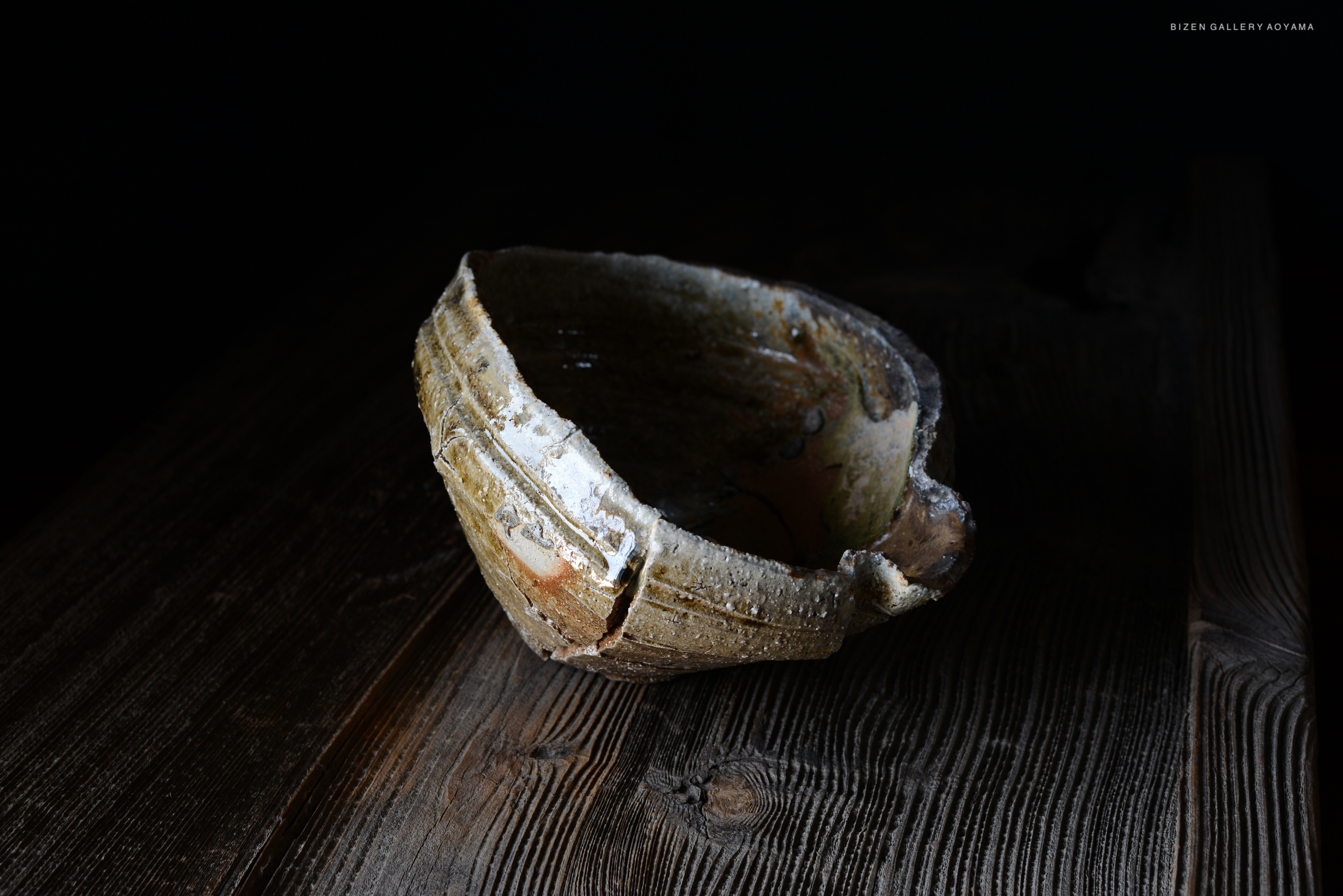 暗い背景に置かれた、独特な形状の陶器のボウル。木製のテーブルの上に置かれている。