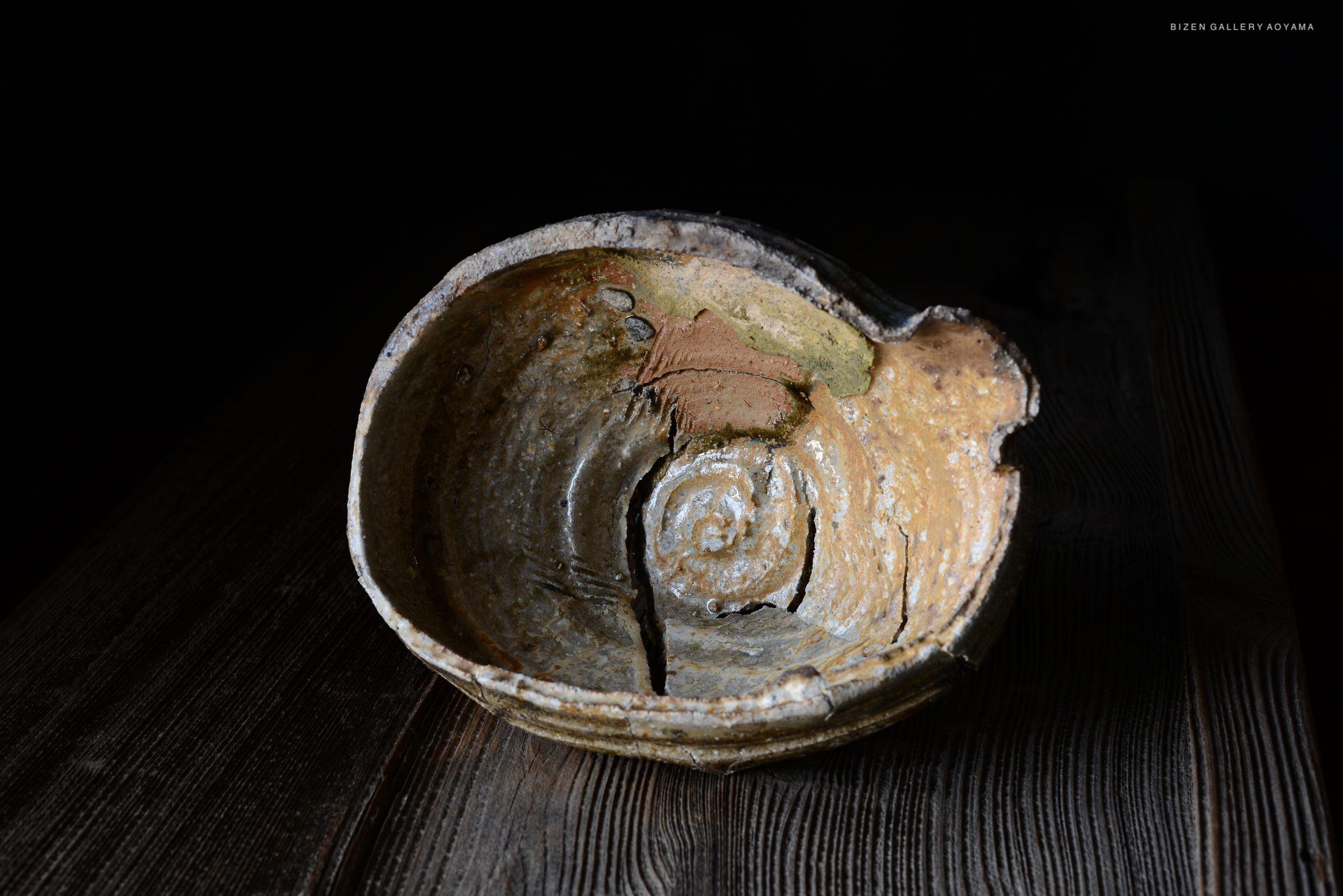 陶器の壺が木のテーブルの上に置かれている。壺は古びた質感を持ち、内部は渦巻き状の模様が見える。