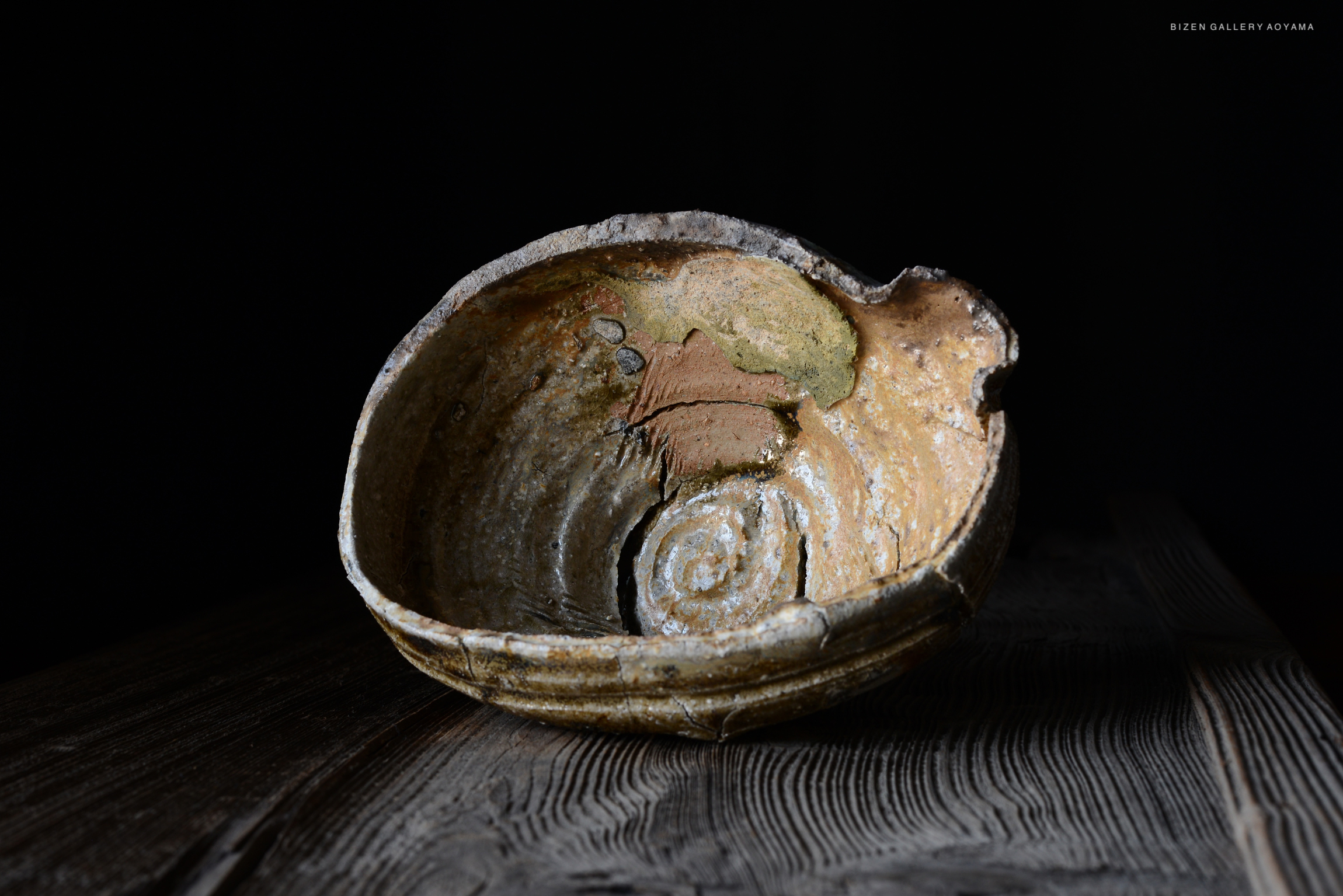 黒い背景に置かれた、独特な形状のビゼン焼きの器。内部にはらせん状の模様と自然な色合いが見られる。