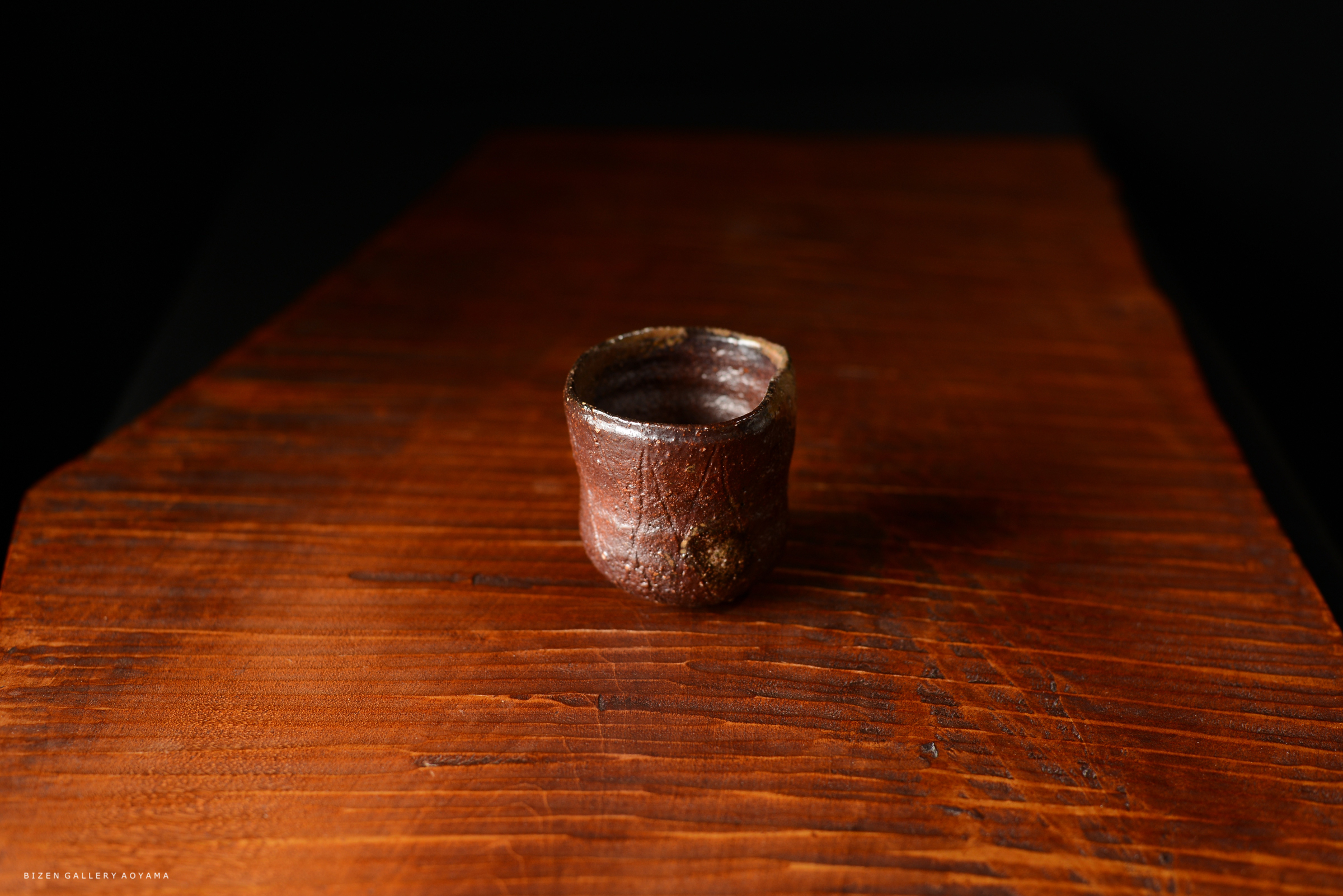 木のテーブルの上に置かれた、焼き物の小さなカップ。