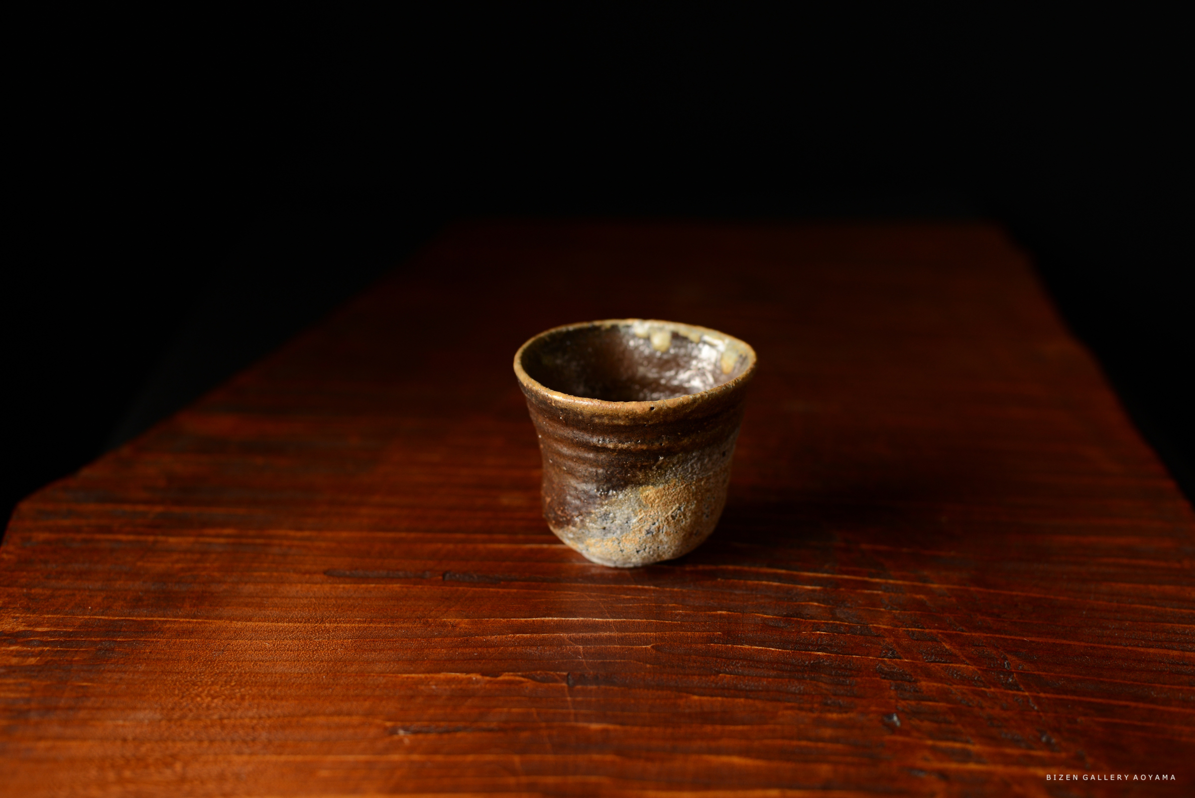 黒い背景の前に置かれた焼き物の小さな陶器のカップ。木製のテーブルの上にあります。