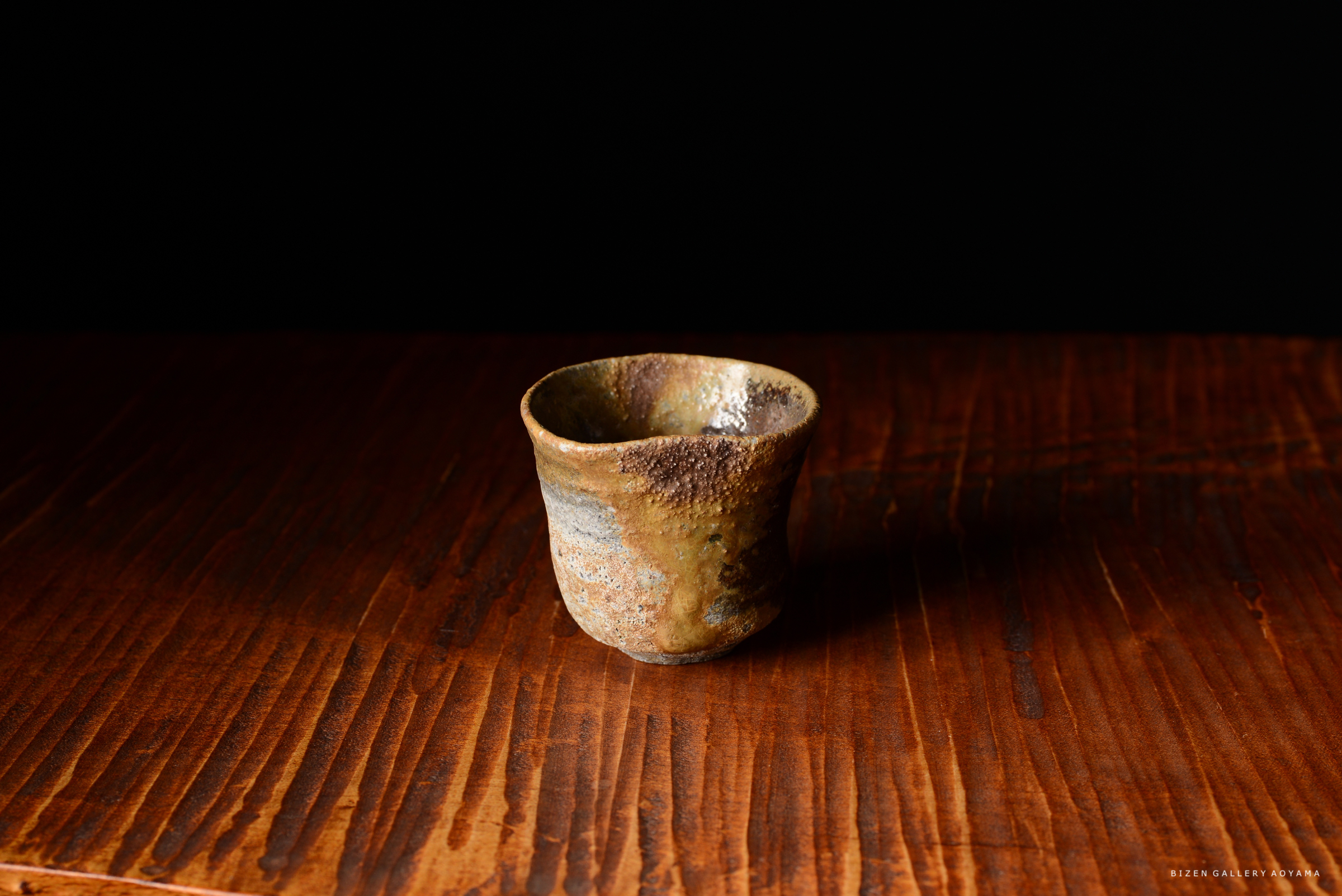 木のテーブルの上に置かれた、陶器のぐい呑み。暗い背景に浮かび上がっている。