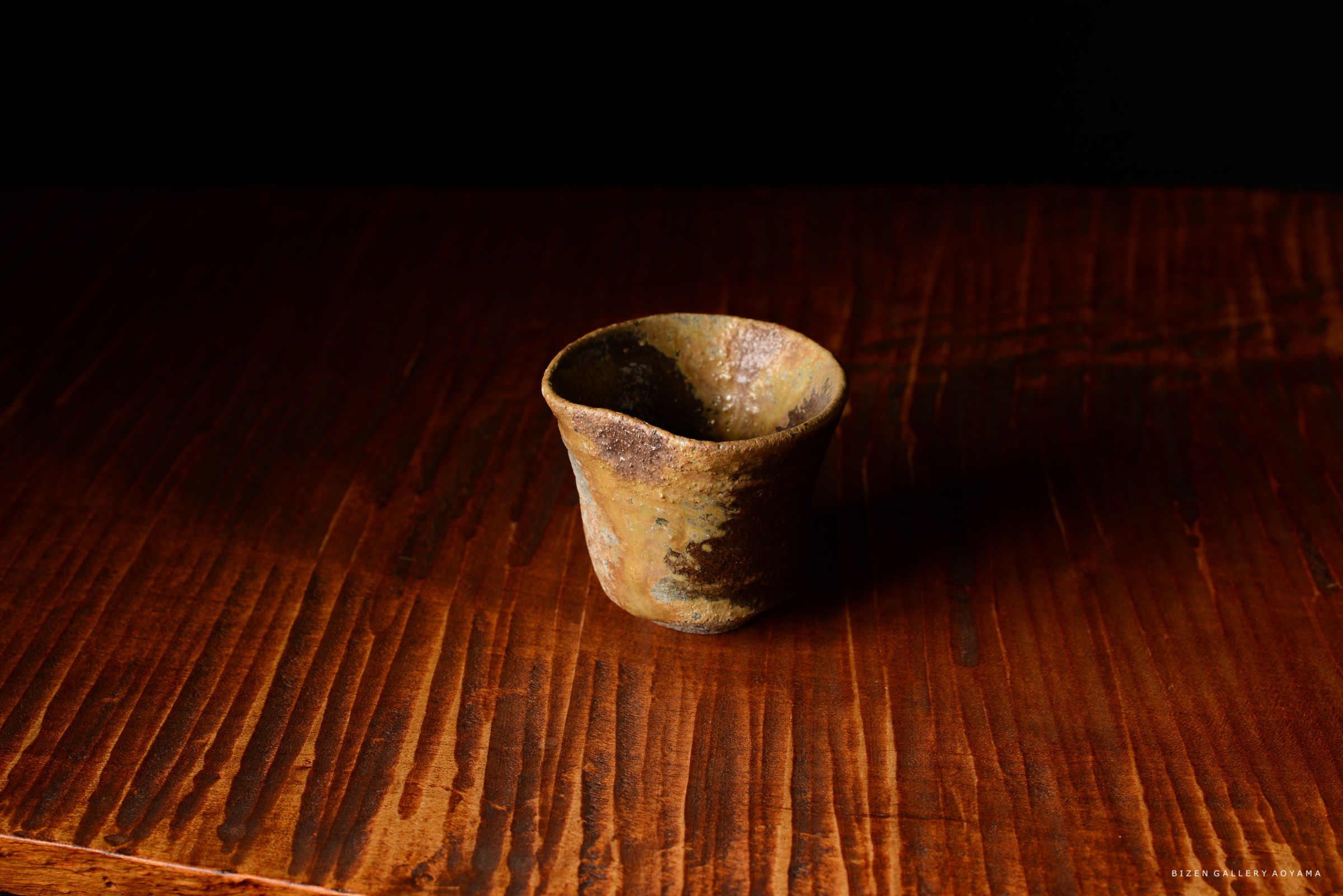 黒背景の前に置かれた古い陶器のカップが、木のテーブルの上にある