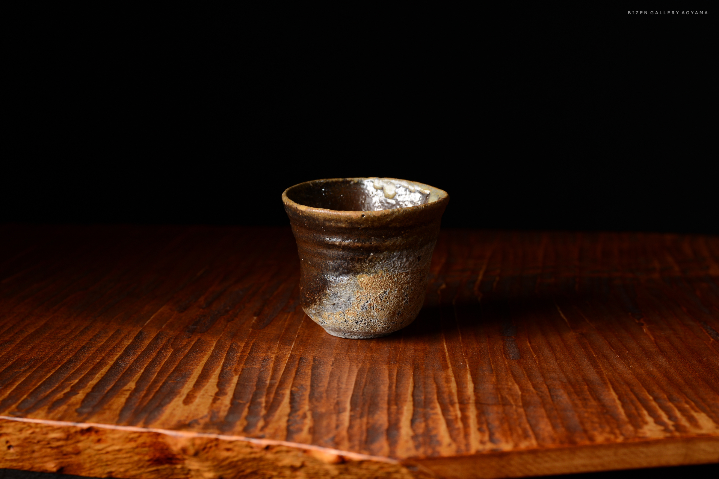 黒い背景の上に置かれた陶器の小さなカップ。木製のテーブルの上にあります。