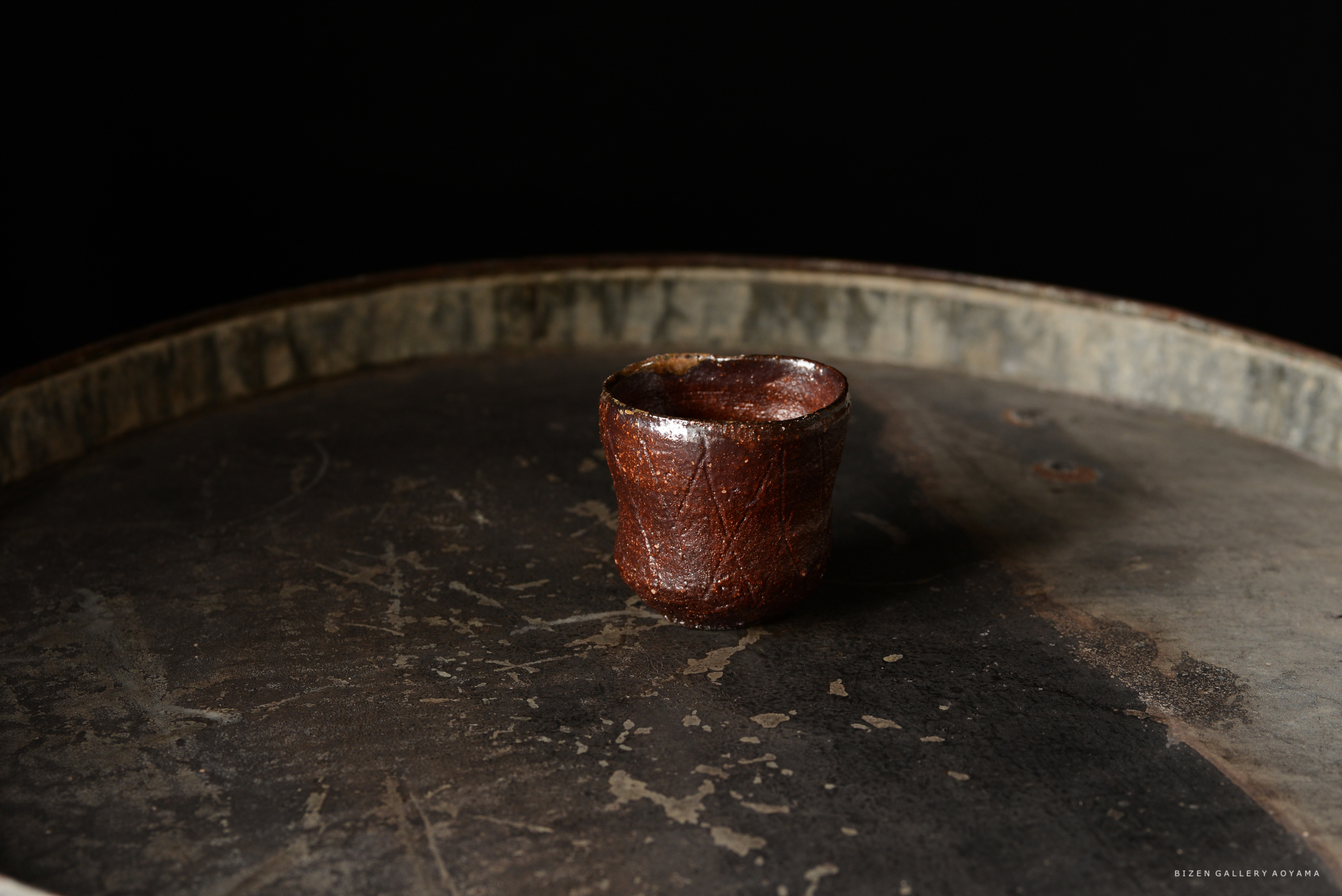茶道具として使われる伝統的な焼き物の小さな茶碗が、暗い背景の上に置かれています。