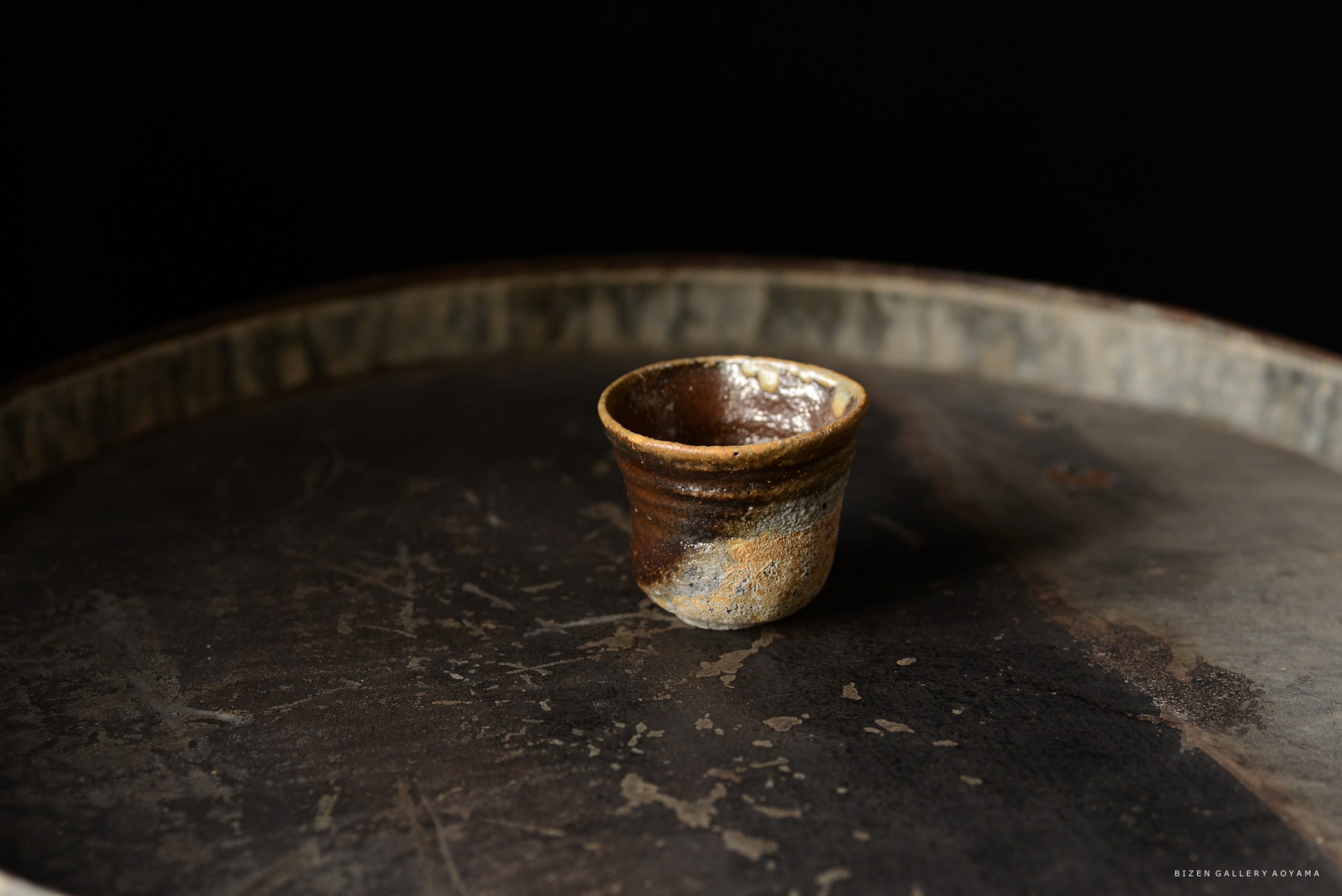 黒い背景の上に置かれた小さな焼き物のカップ。カップは自然な色合いで、手作りの風合いが感じられる。