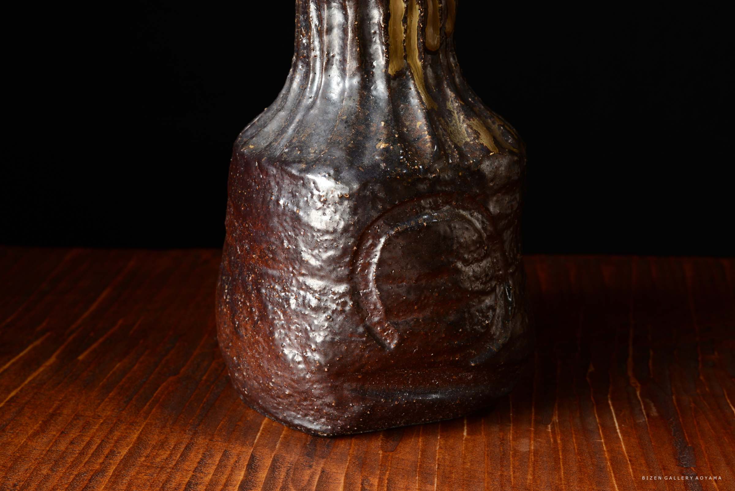 ザラザラした表面を持つ茶色の陶器の壺が、木のテーブルの上に置かれている。