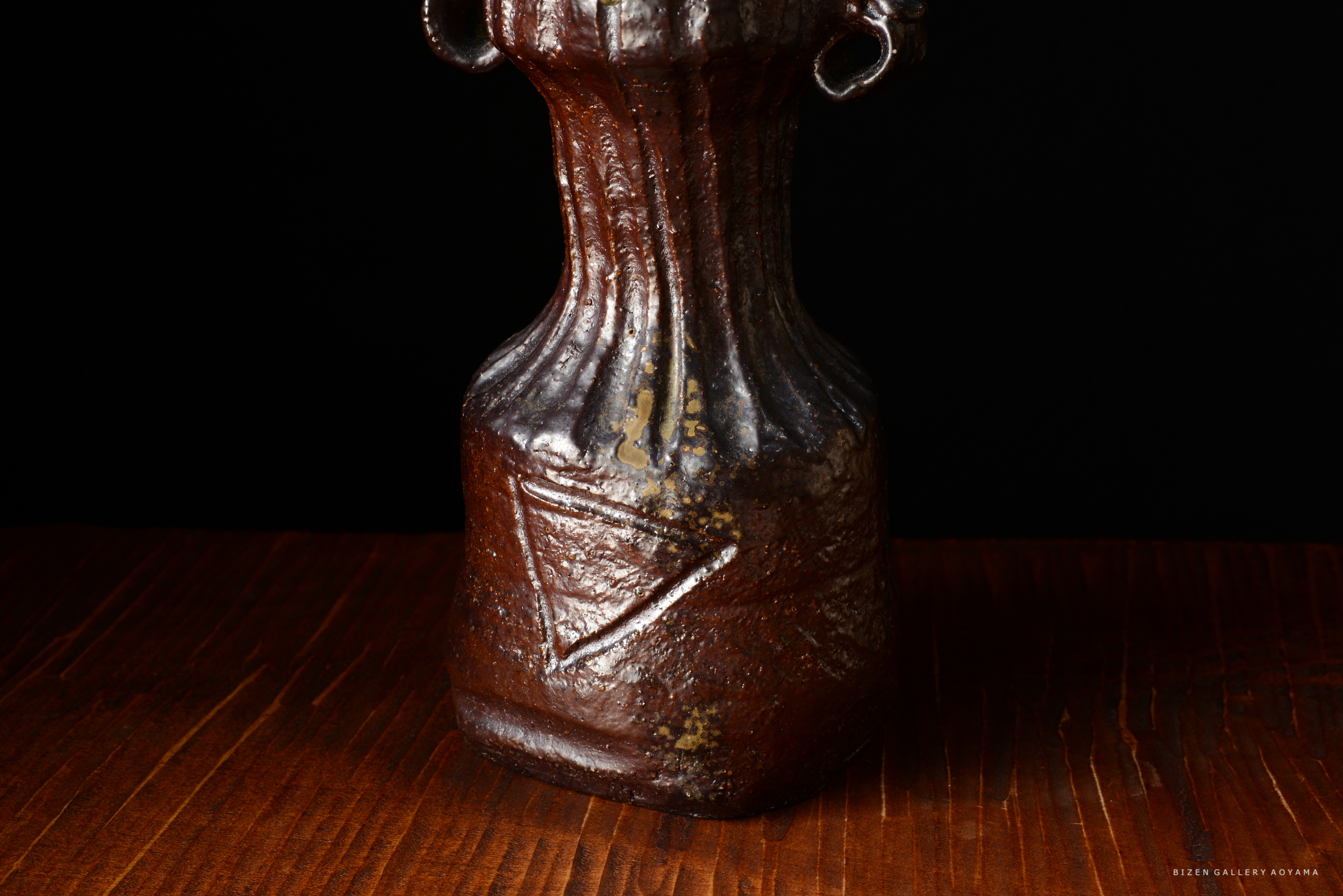 暗い背景に対して、独特な模様が施された陶器の花瓶。木製のテーブルの上に置かれている。